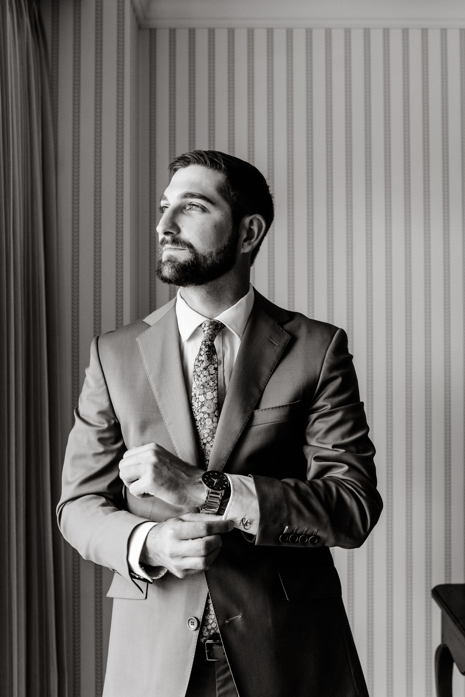 Series of black and white photos showing a man in a suit adjusting his tie and jacket during wedding preparations.