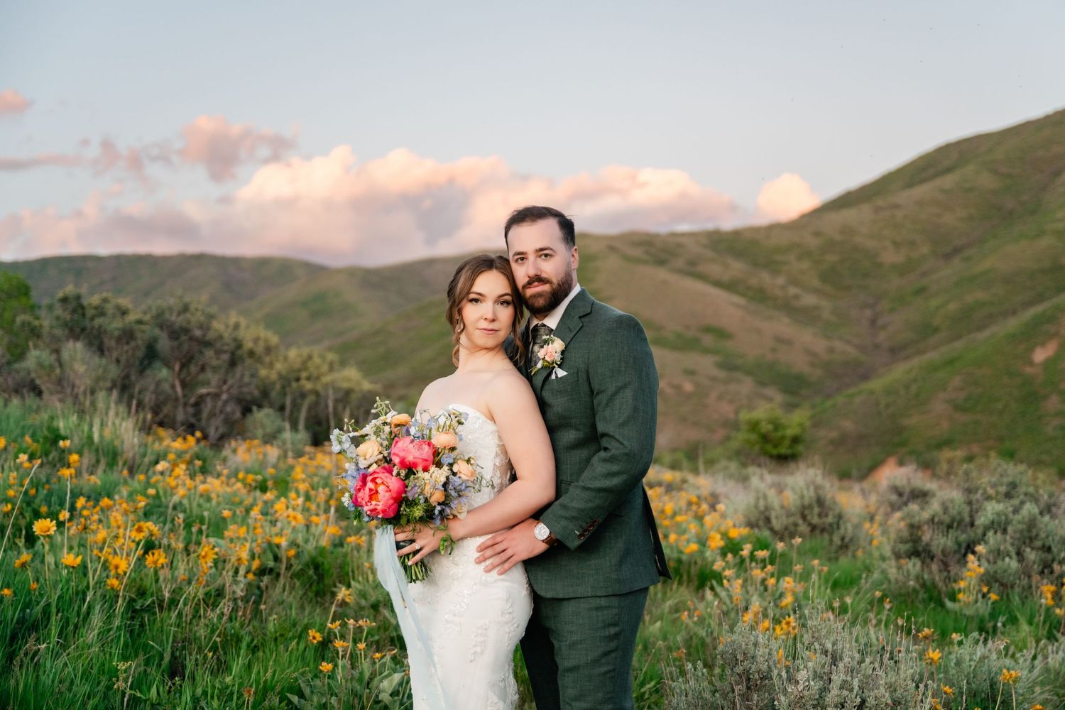 Wedding portraits in mountain landscape with dramatic sunset sky and yellow wildflowers.