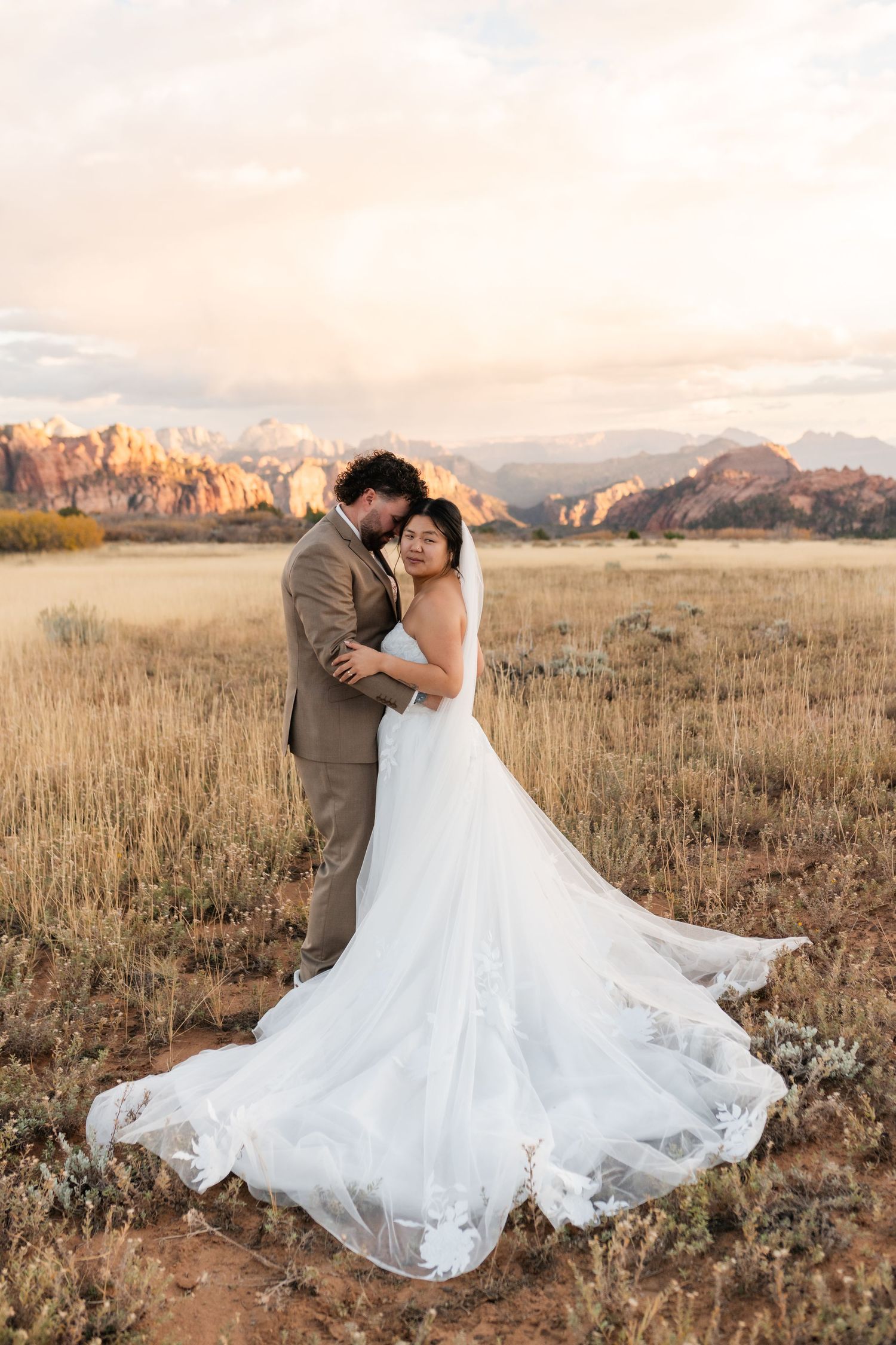 A wedding couple dances in a rustic field with flowing white dress against a backdrop of majestic mountains.