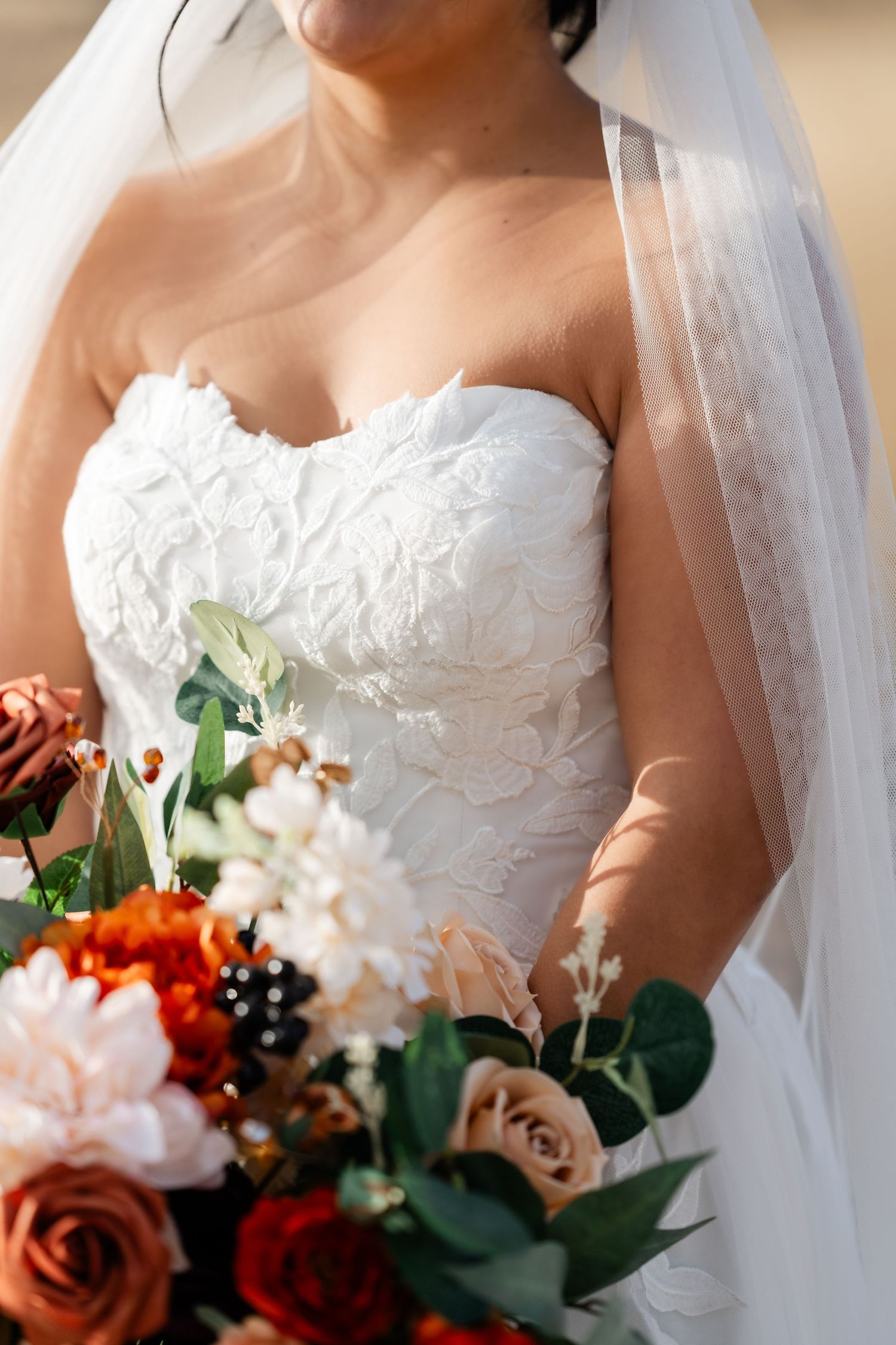 Close-up detail of white lace wedding dress and colorful autumn bouquet.