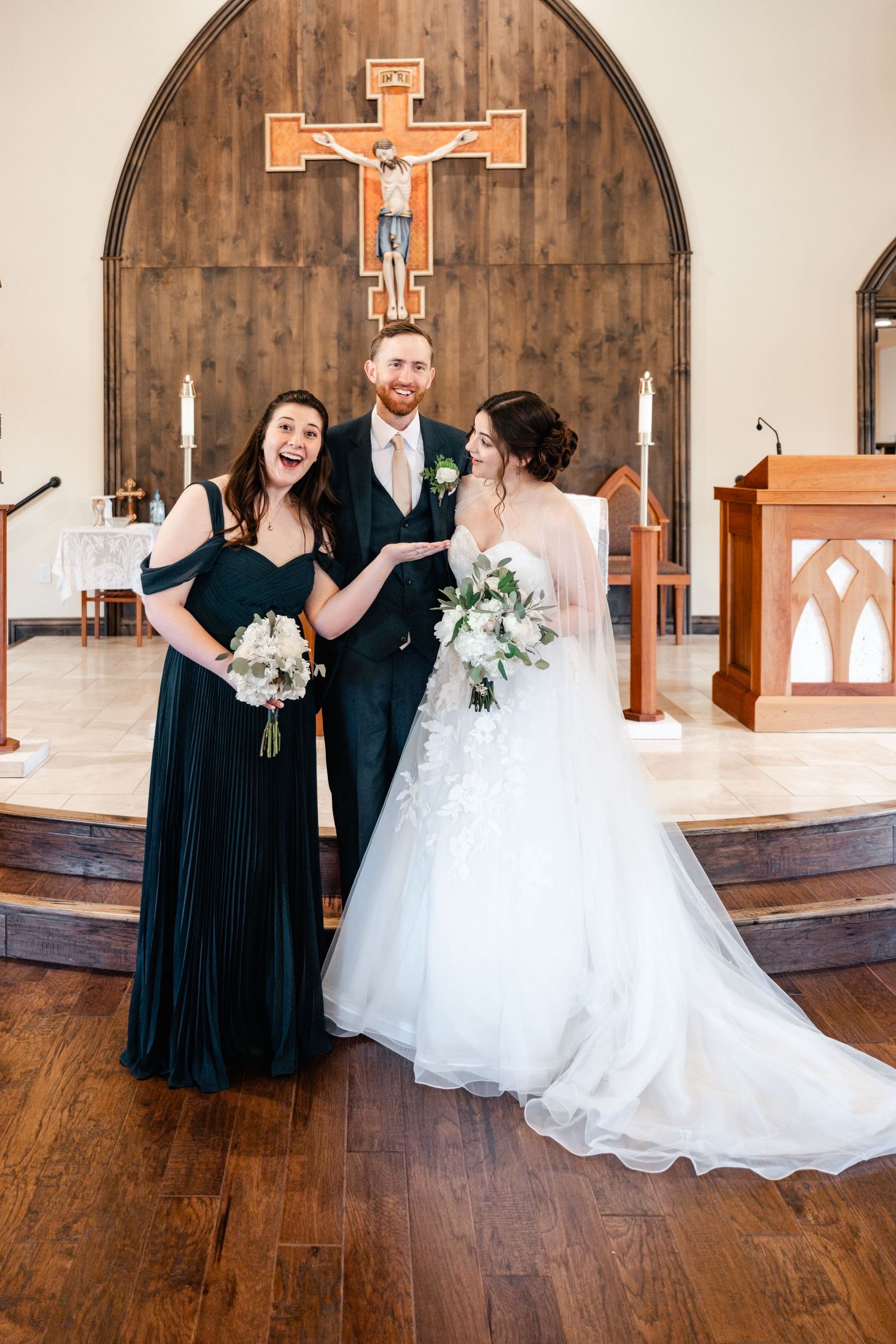 Wedding group shares joyful moment in church sanctuary with wooden cross and white candles.