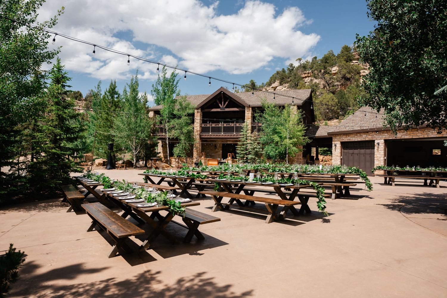 Mountain lodge venue with picnic tables and string lights under blue sky.