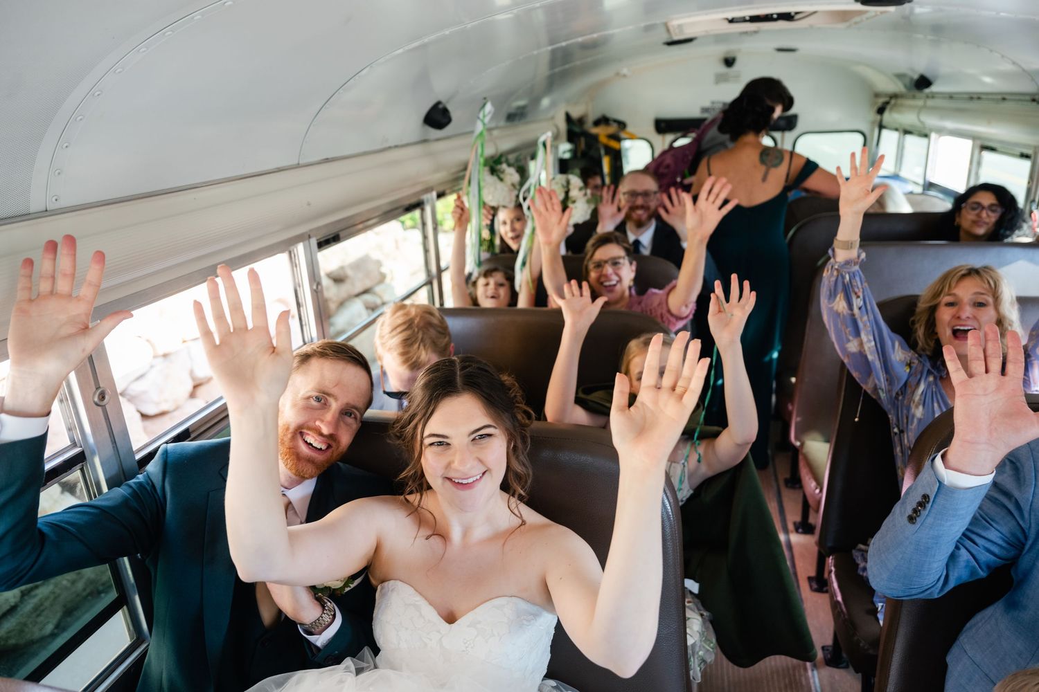 Wedding party celebrates joyfully with raised hands while riding in a party bus together.