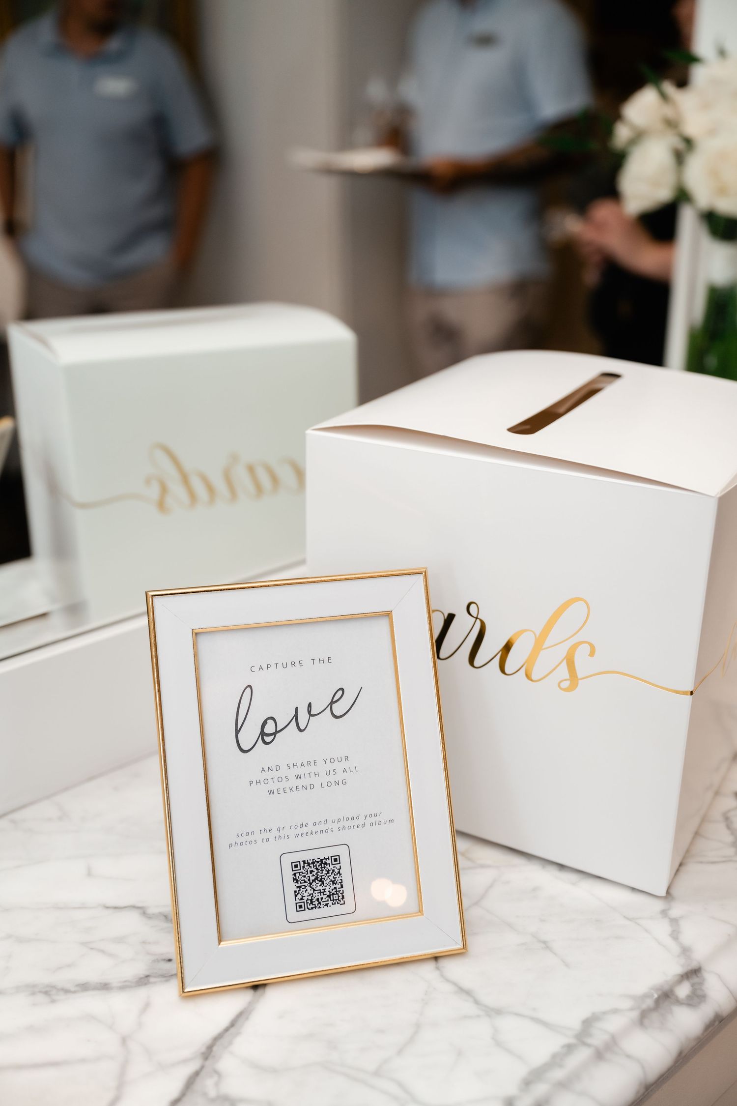 White gift boxes with gold trim and elegant text arranged on a marble surface at a wedding.