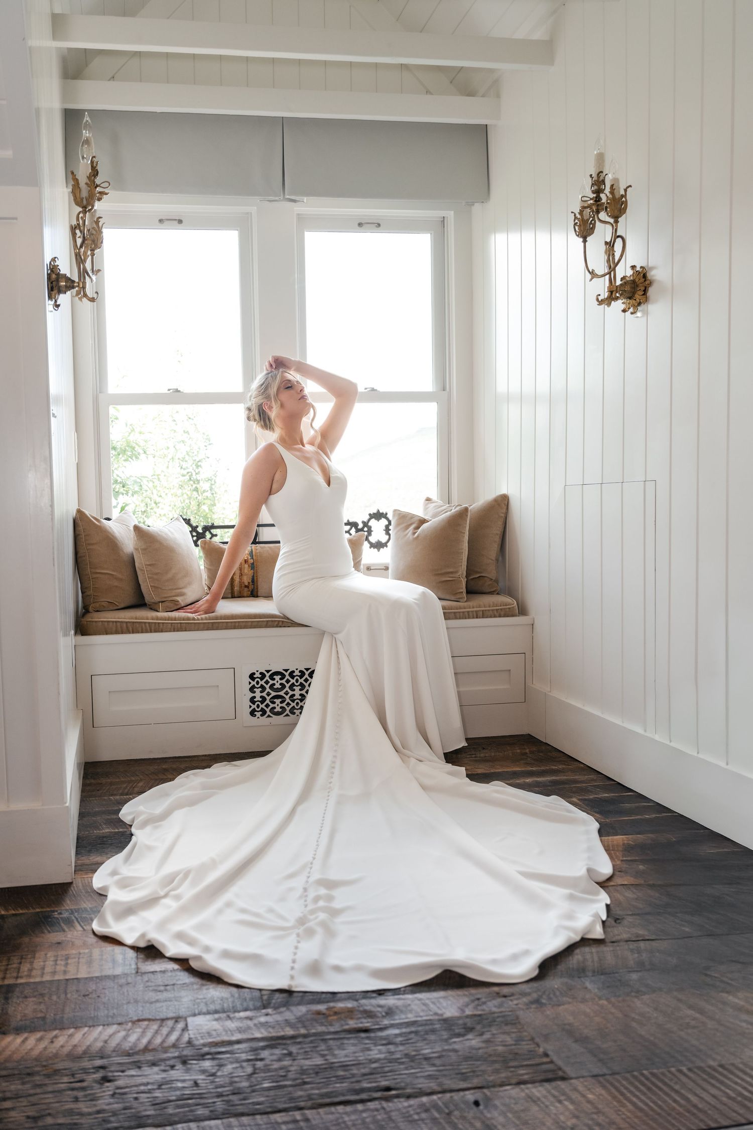 Flowing white wedding gown displayed in a bright sunlit room with rustic wooden floors.