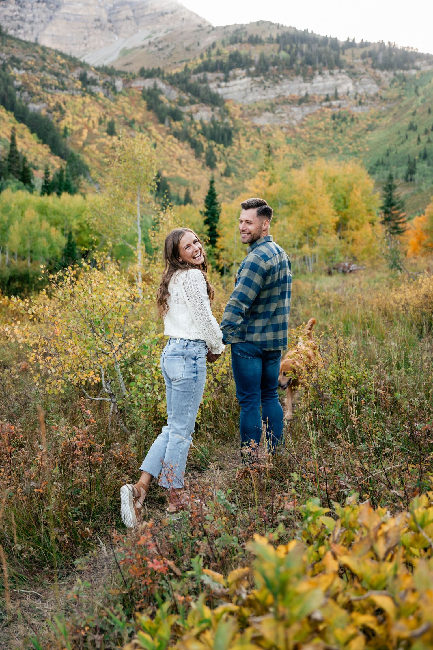 A couple shares a moment together on a mountainside trail surrounded by vibrant fall foliage in the wilderness.