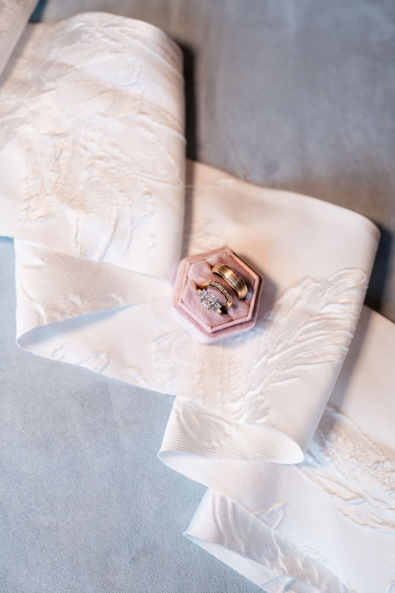A pink hexagonal ring box sits atop folded white fabric with delicate embroidery details. Park City Wedding Photographer. Utah Wedding