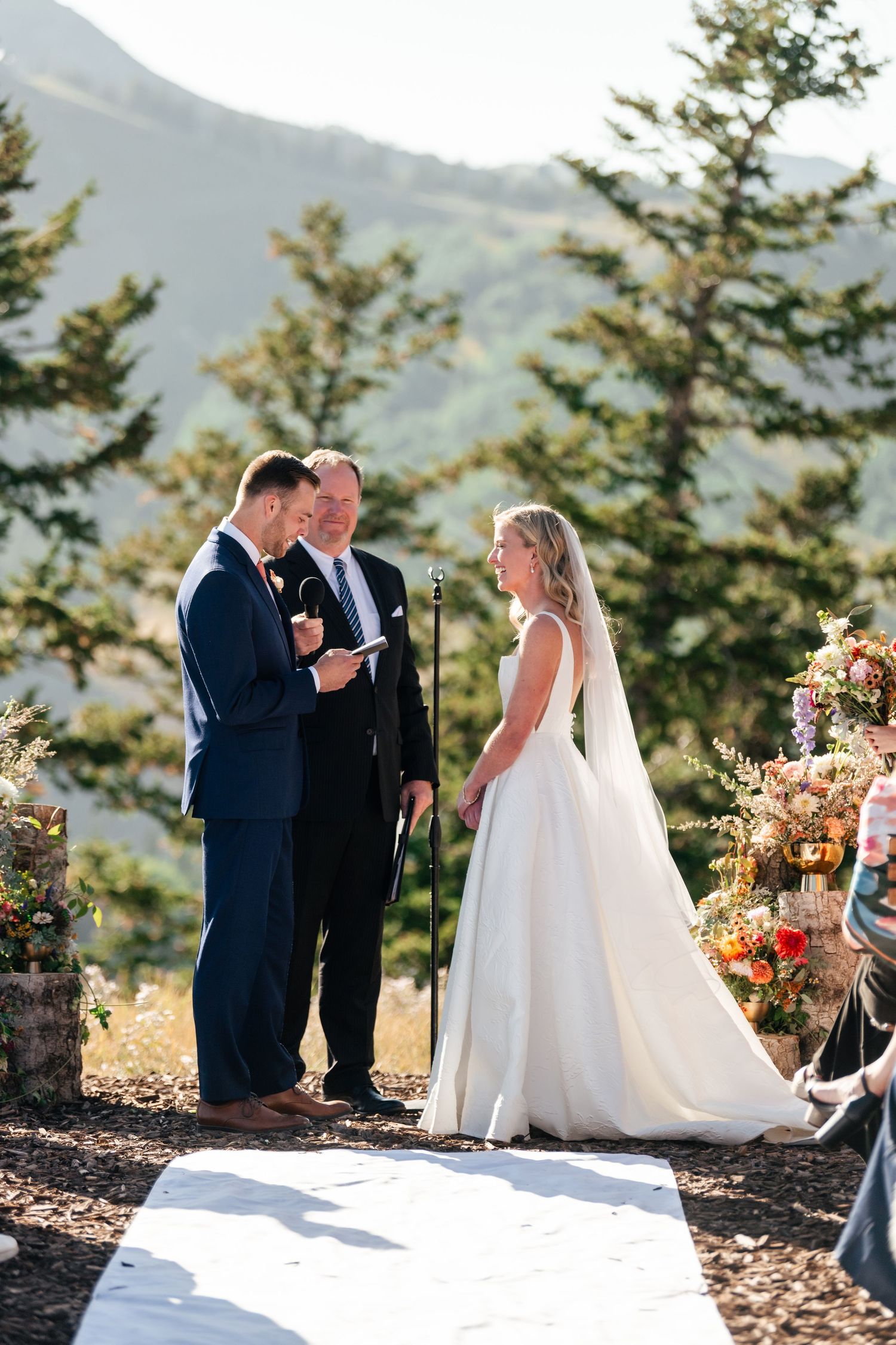 A wedding ceremony takes place on a mountaintop with evergreen trees and scenic views in the background. Park City Wedding Photographer.