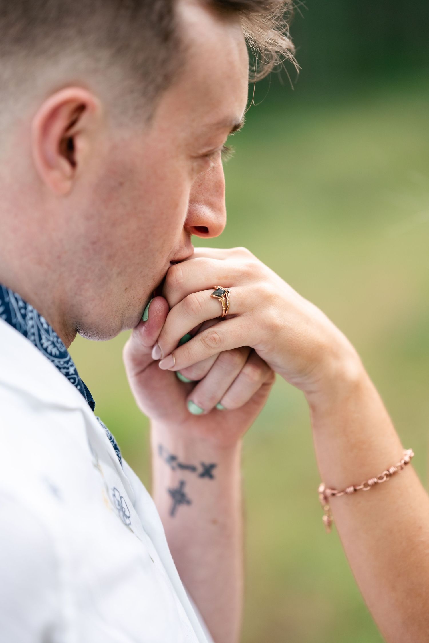 Close up of hands with engagement ring and tattoo as man kisses partner's hand outdoors. Park City engagement photographer.