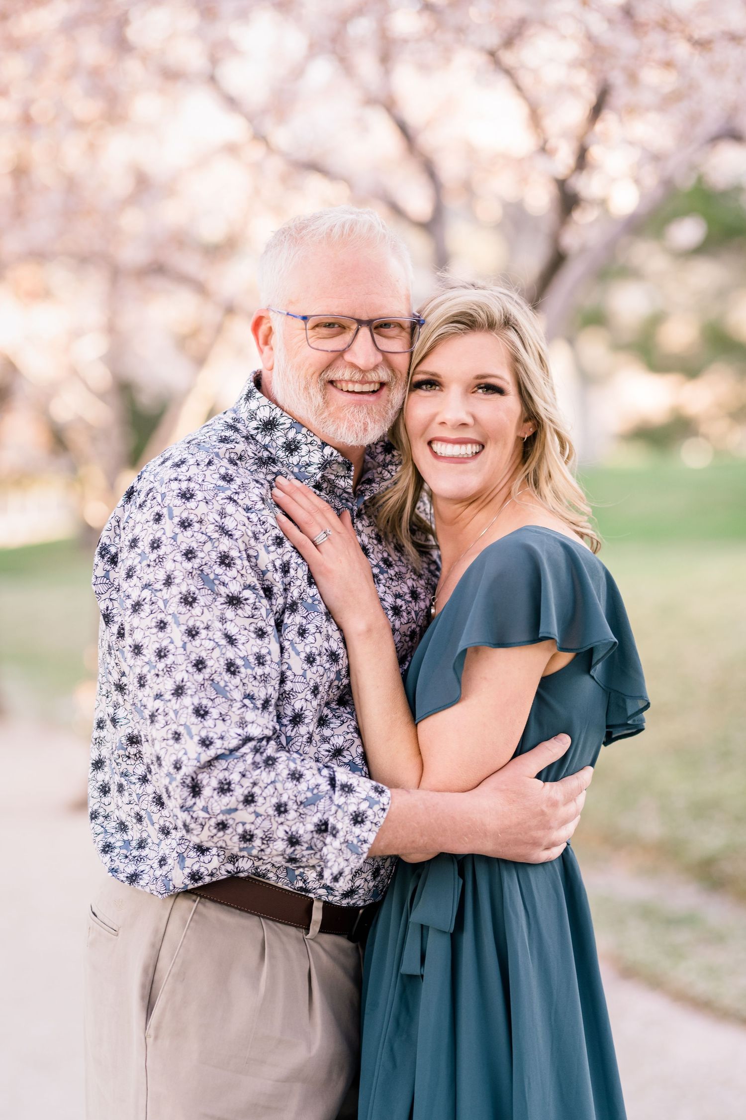 Happy engaged couple snuggling close and smiling to the camera the the blossoms at the Capitol building by Coley Cook
