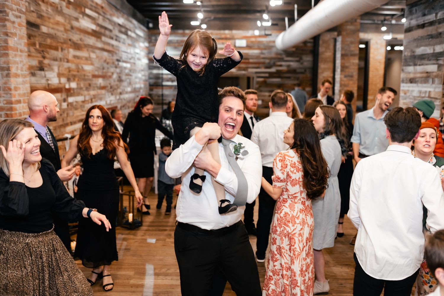 A crowd of people dancing and celebrating at a party in a rustic brick-walled venue.