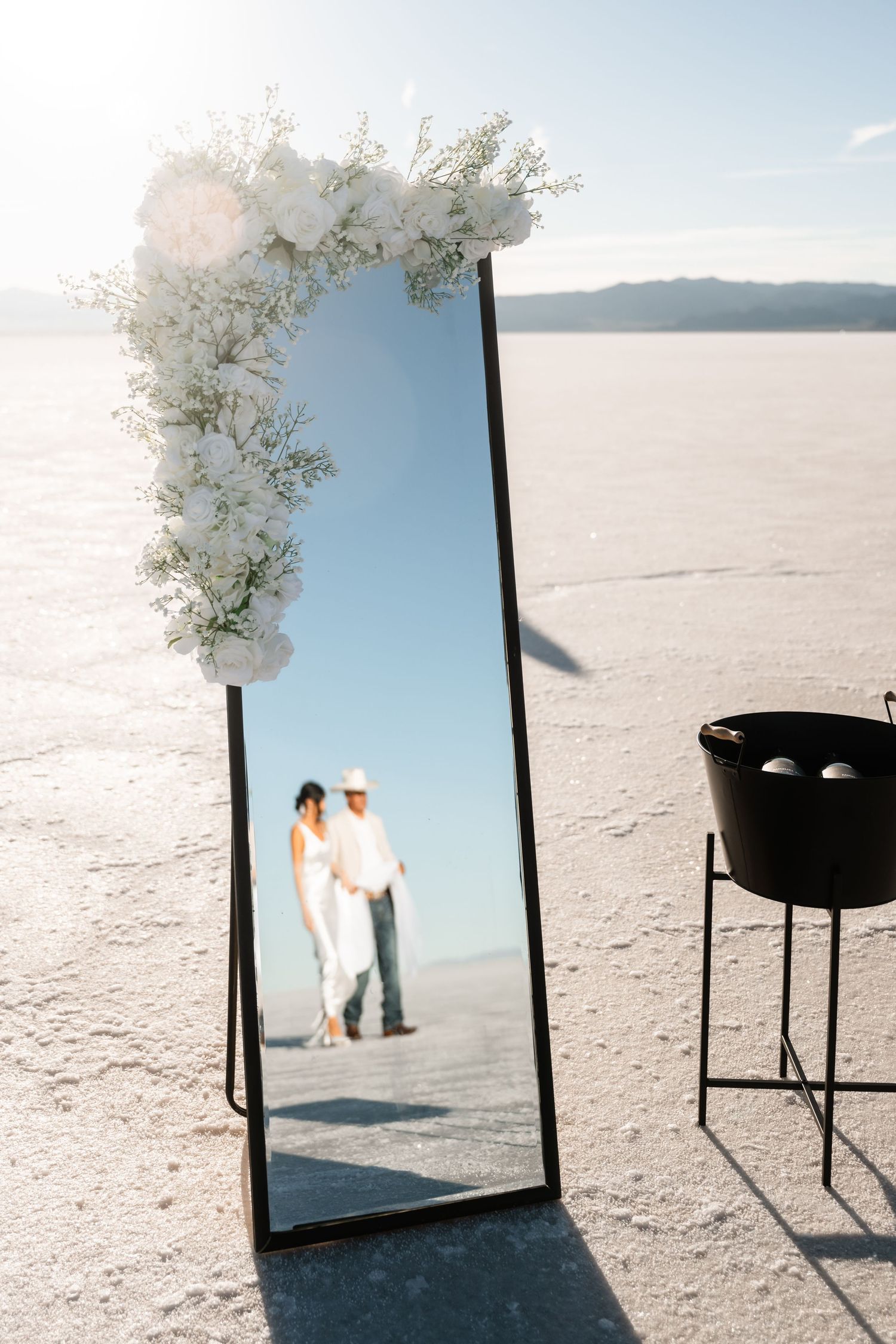 Wedding ceremony setup with mirrors reflecting a desert landscape and white floral arrangements.