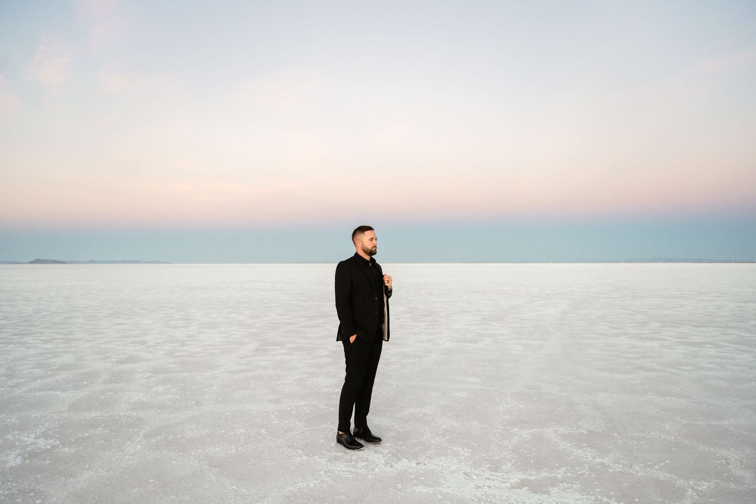 A solitary figure stands on the vast expanse of the Bonneville Salt Flats under a clear blue sky.