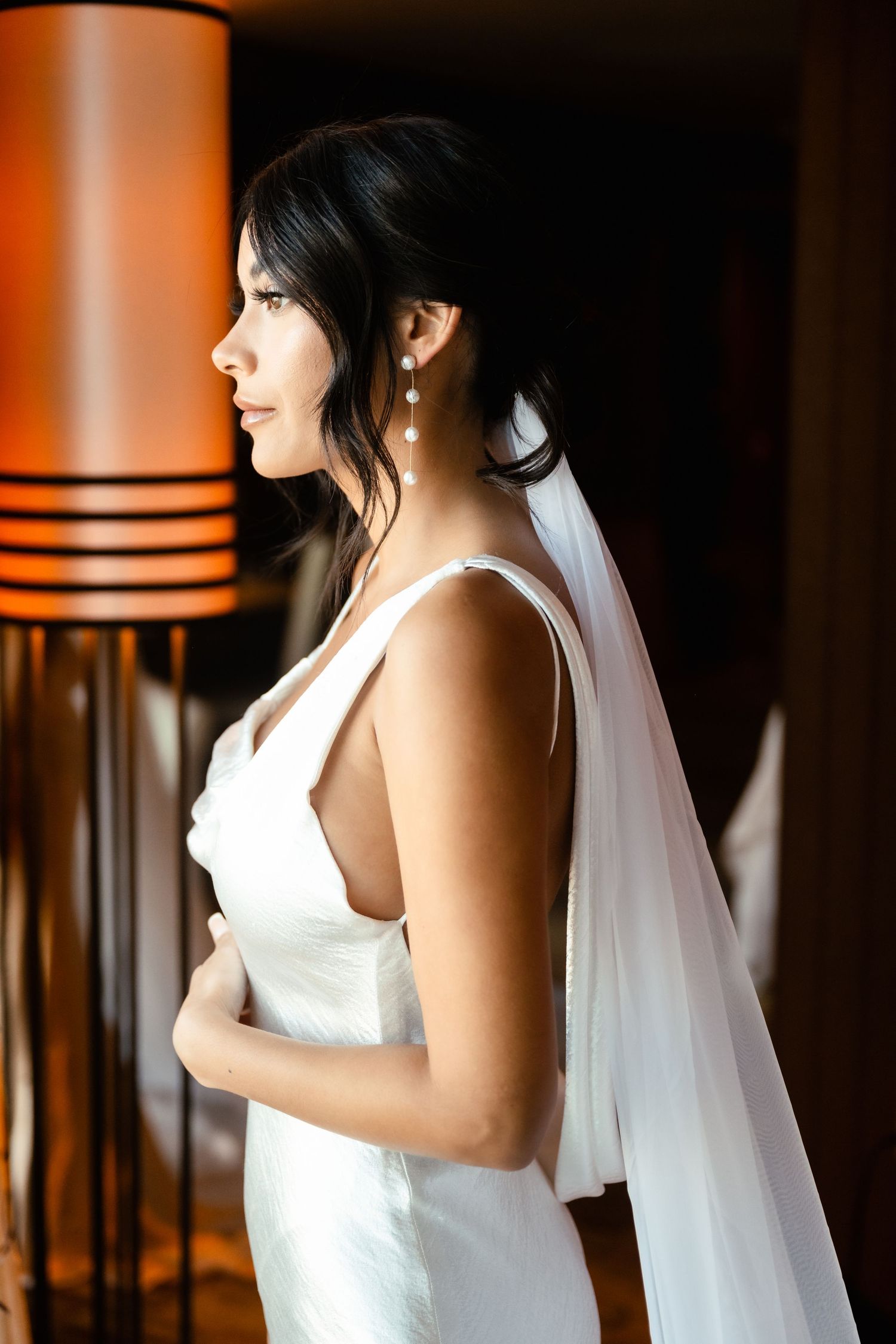 Close-up profile view of a bride in a white wedding dress and veil against a warm-toned background.