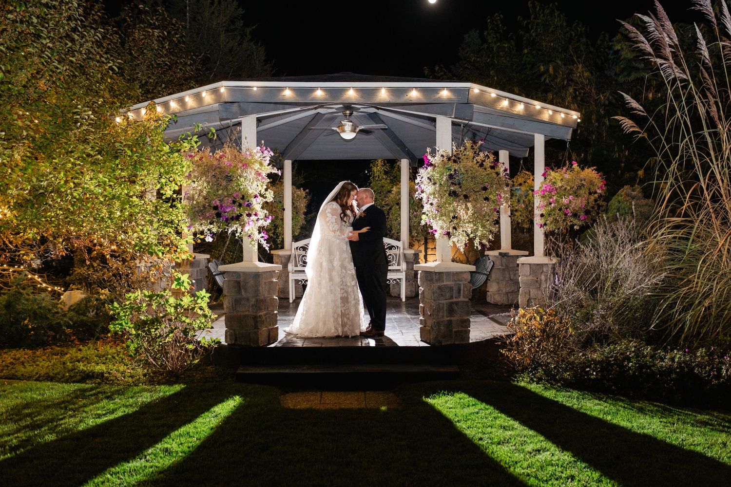 A romantic evening wedding ceremony under an illuminated gazebo surrounded by lush garden landscaping. Millennial Falls photographer.