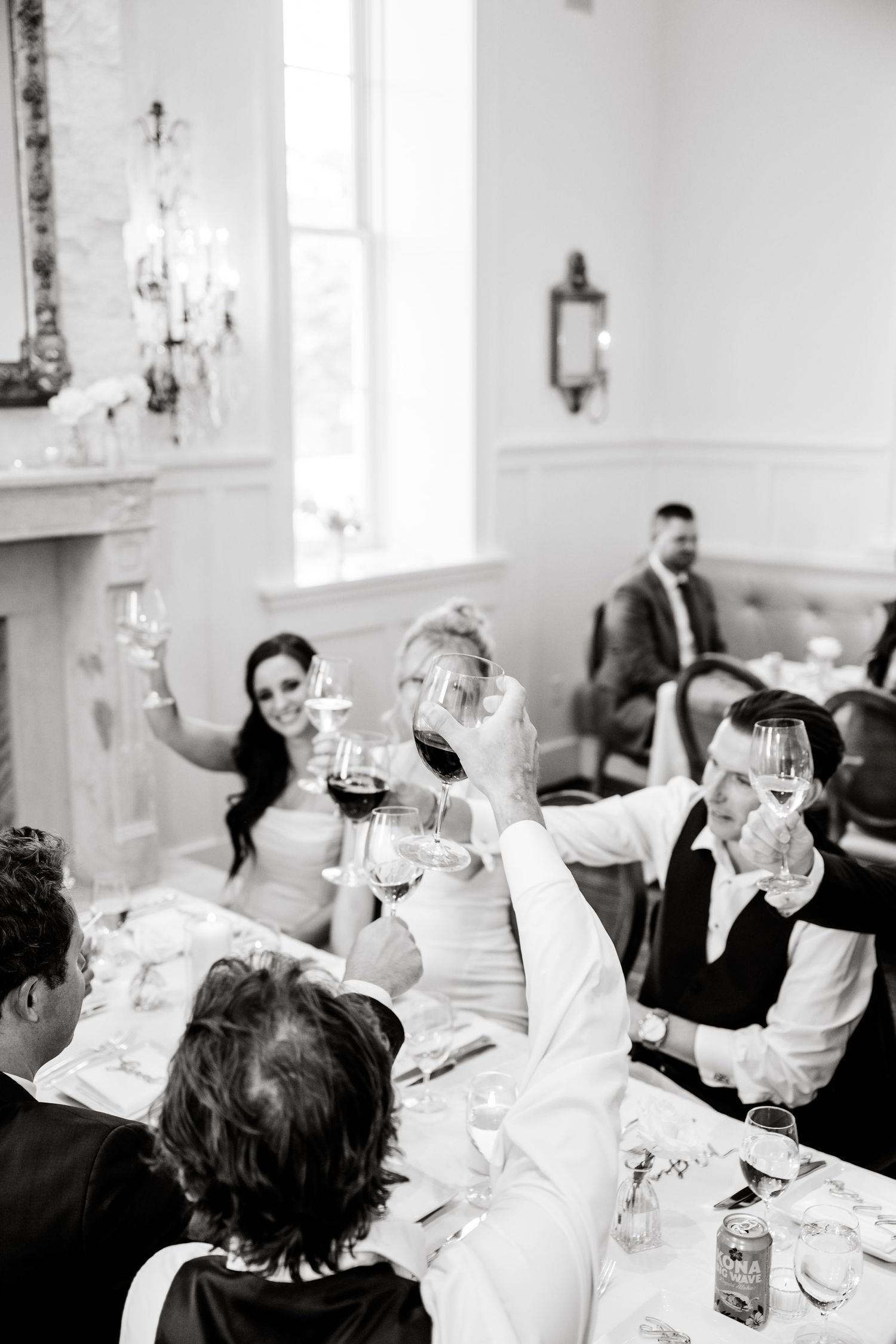 Wedding reception guests raise their glasses in a toast inside an elegant white-walled venue.