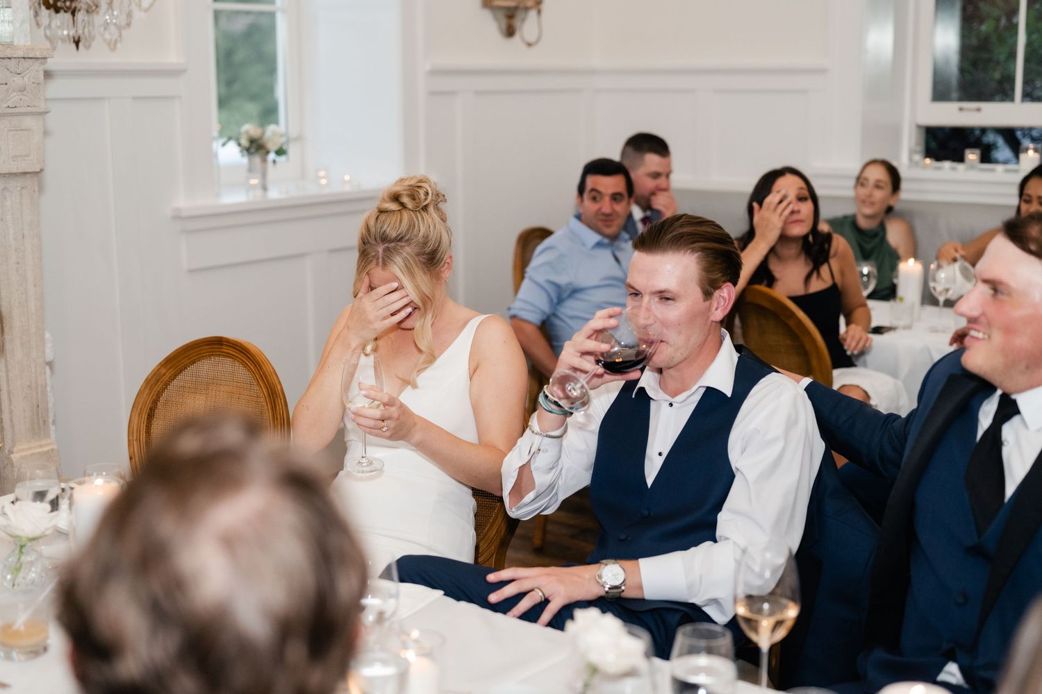 Wedding guests laugh and socialize during an elegant indoor reception dinner.