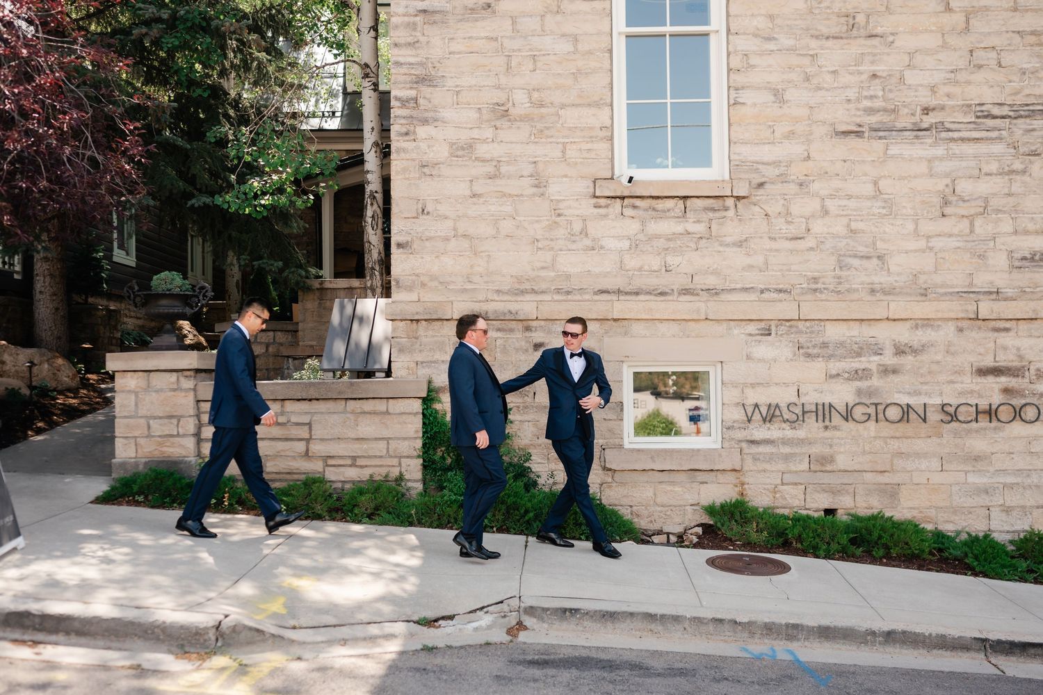 People in formal attire walking along the exterior of a stone building.