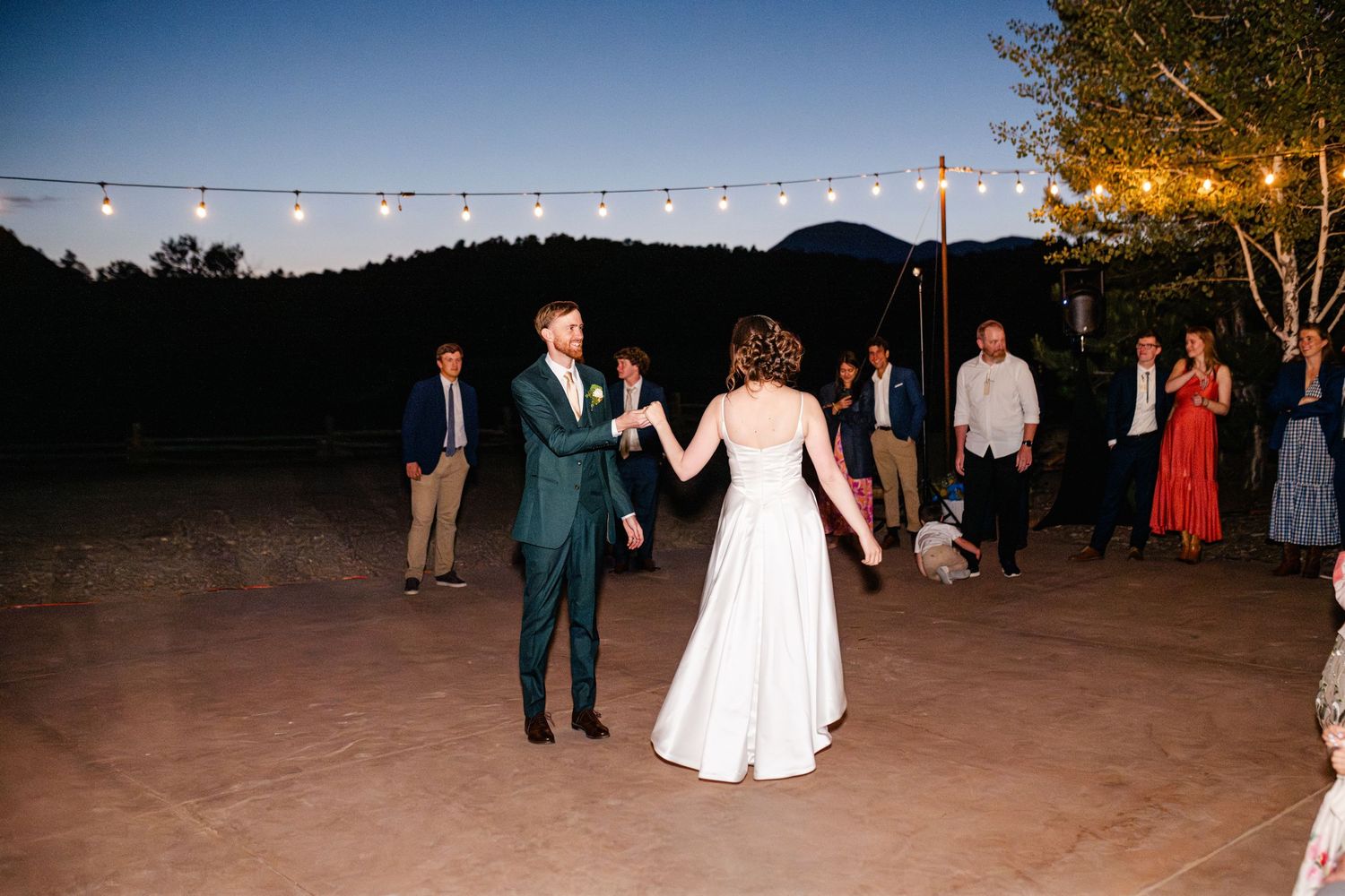 Wedding reception dance floor with string lights and guests celebrating at dusk.