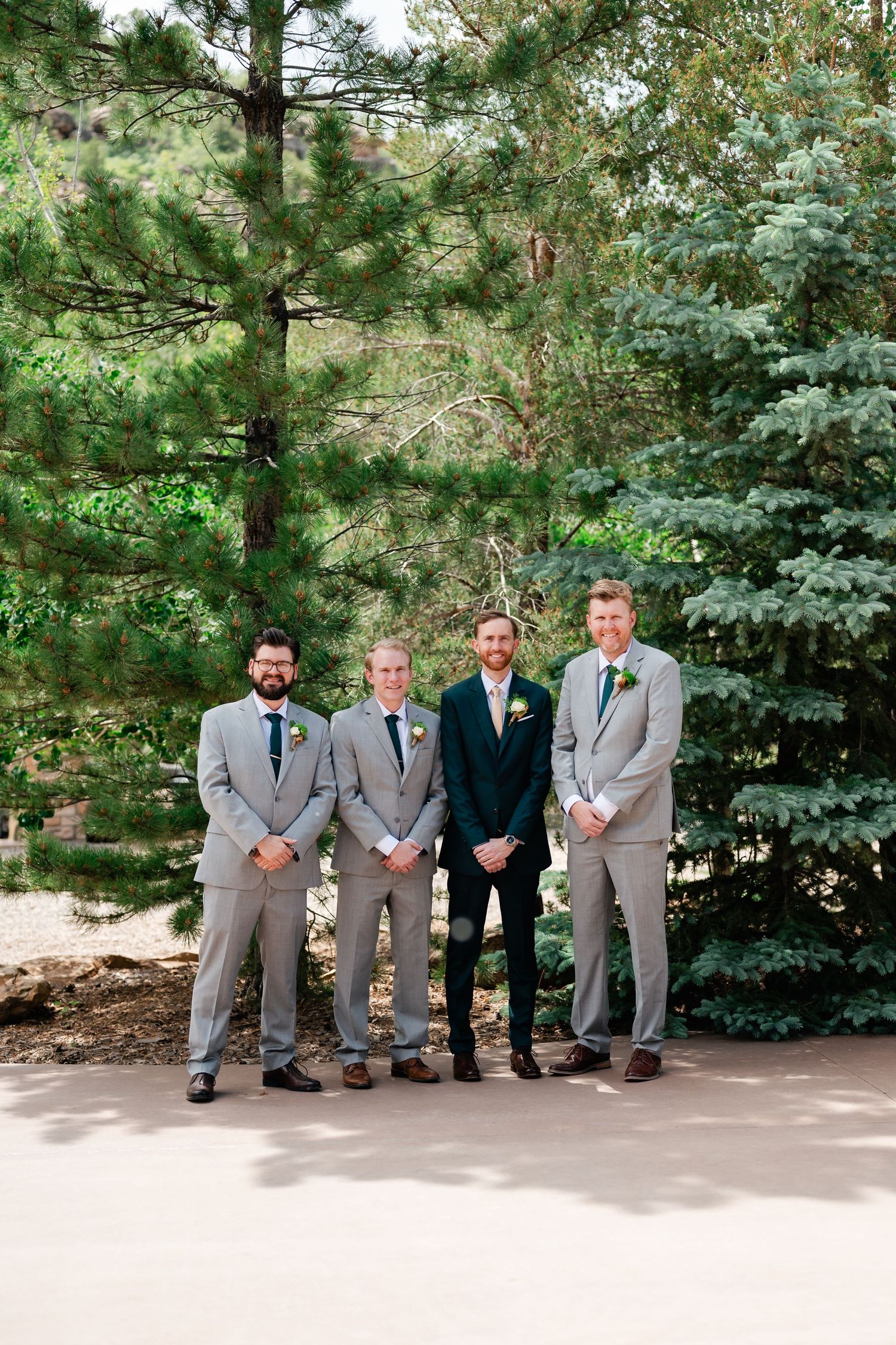 Wedding party in gray suits and navy accents posed casually outdoors against evergreen trees.