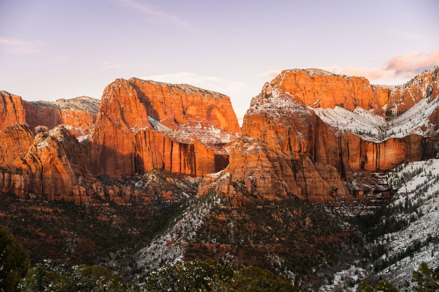 Panoramic view of snow-capped red rock cliffs and canyons at sunset.