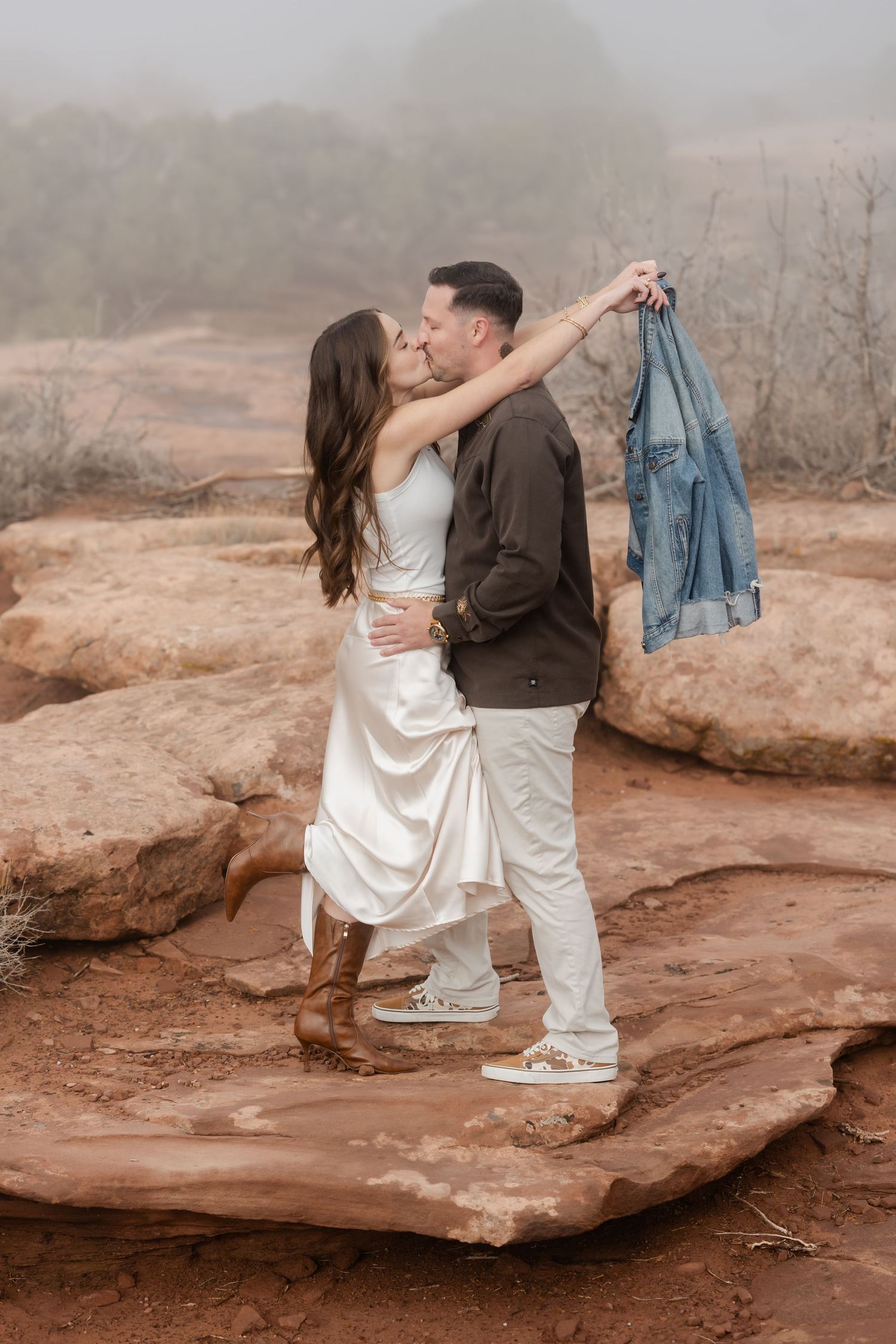 A couple dances romantically on red rock formations in a desert landscape during a photo shoot.
