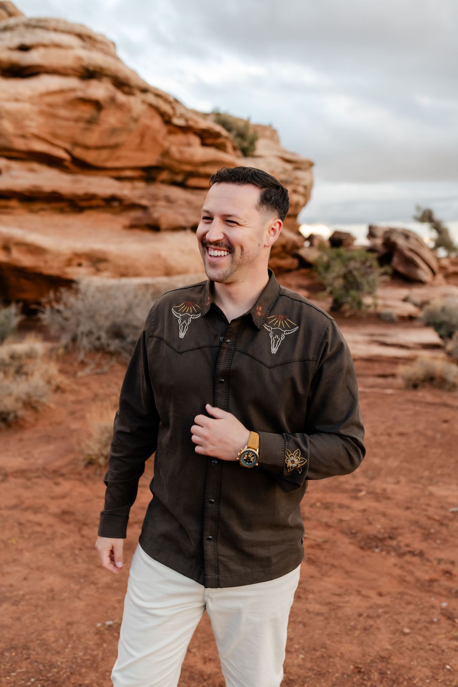 A person in western attire laughs joyfully against a backdrop of red desert rocks.