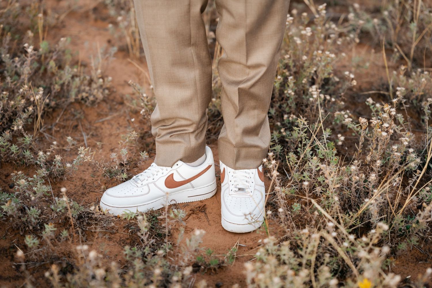 Close-up view of brown leather boots against a rustic outdoor background with dried vegetation.