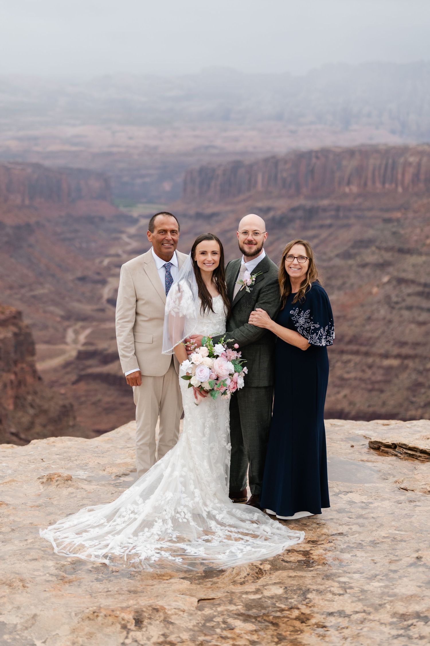 Small wedding group poses for photos on a rocky overlook with sweeping canyon views in the background.