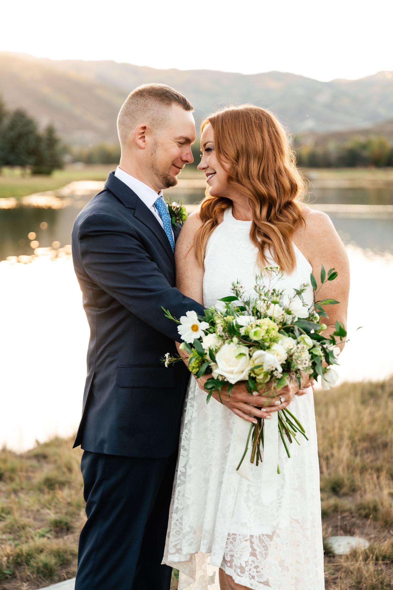 A couple shares an intimate moment by a lake with mountains in the distance.