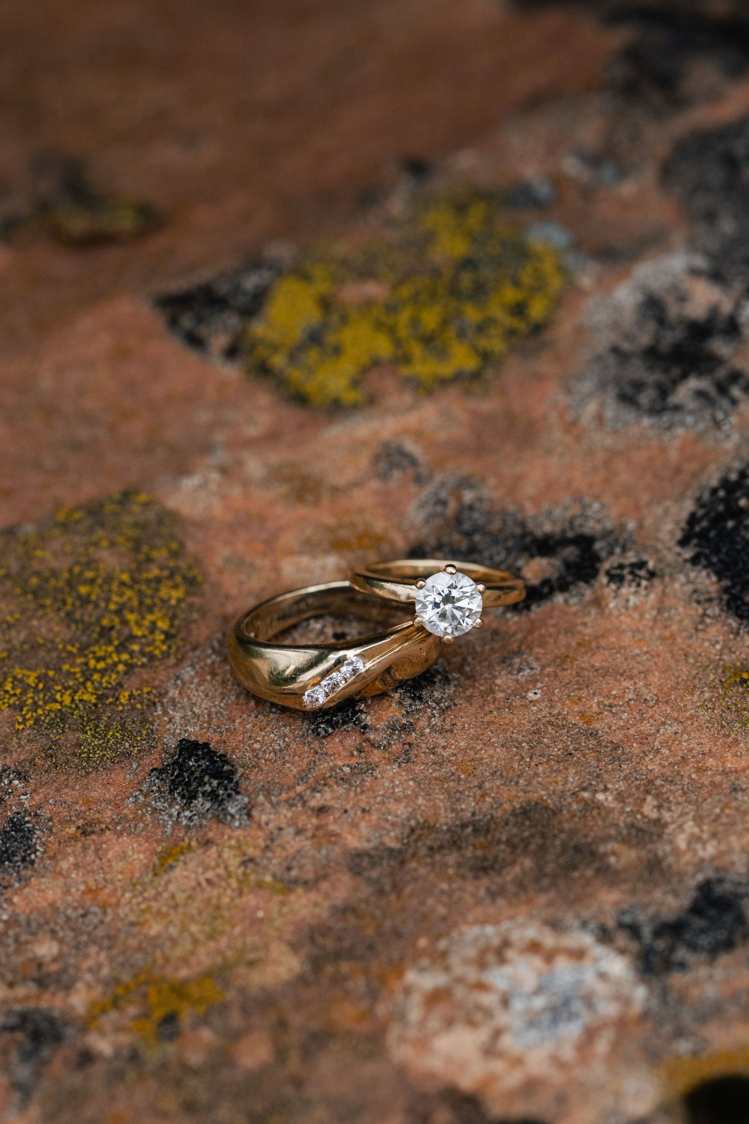 Gold engagement ring with diamond solitaire photographed on textured stone surface.