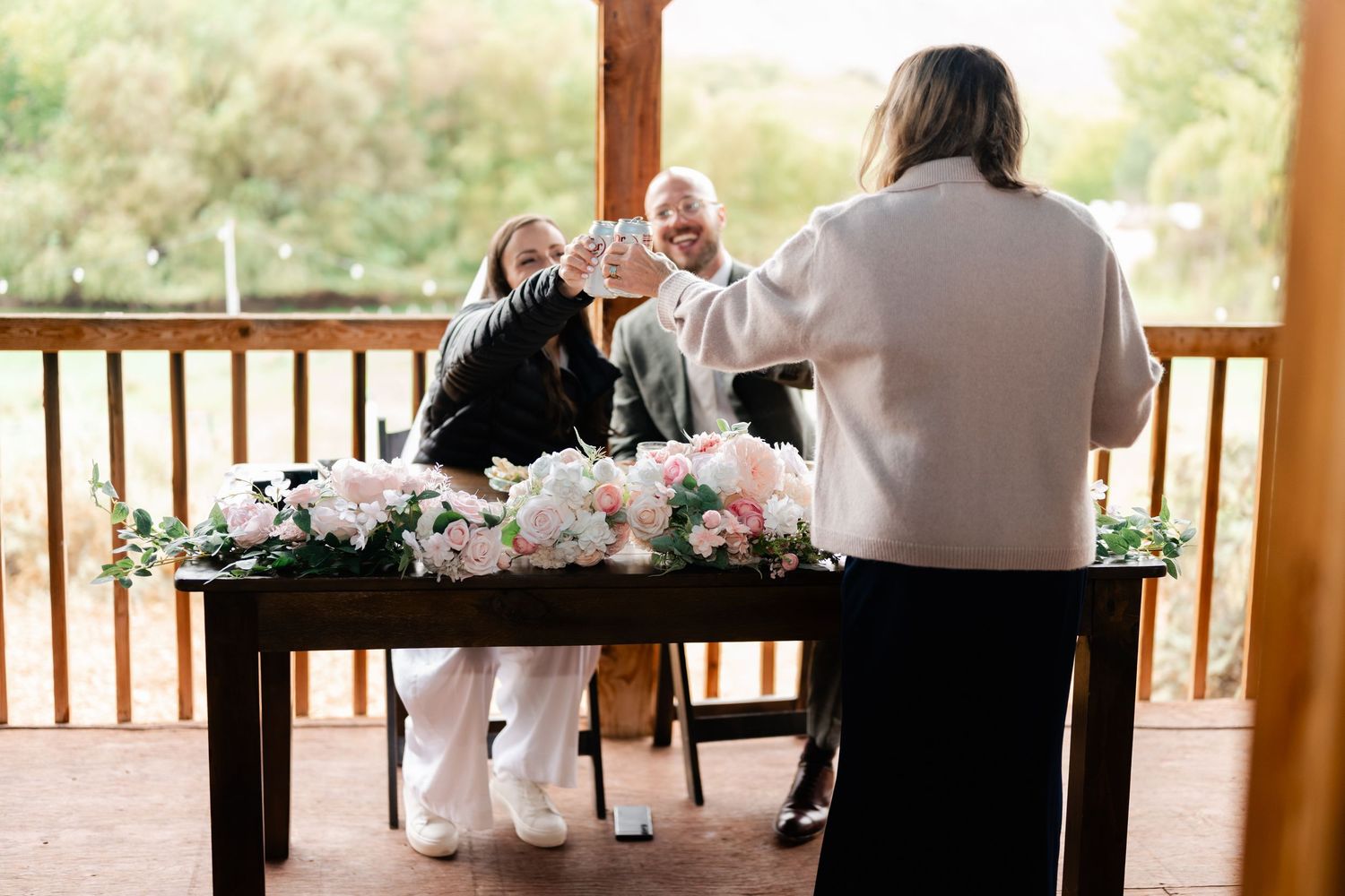 Wedding reception table decorated with pink floral arrangements on a covered outdoor patio.