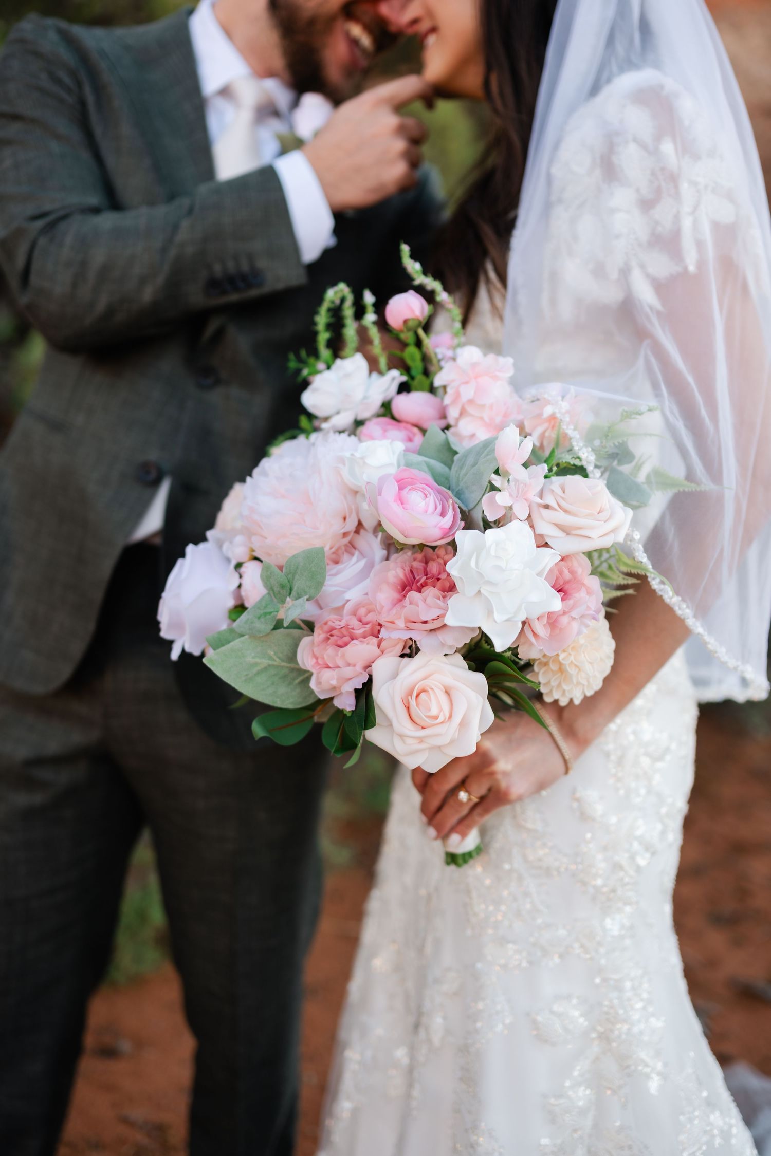 Wedding bouquet with soft pink roses and white flowers held against a lace white wedding dress.