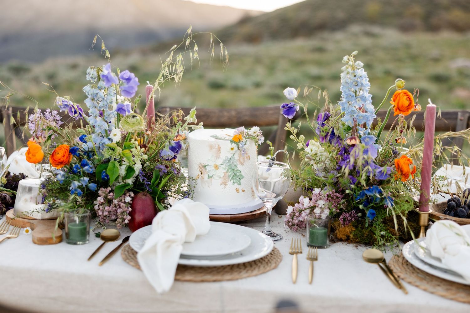 Rustic outdoor wedding table settings with colorful wildflowers and delicate place settings against a natural landscape.