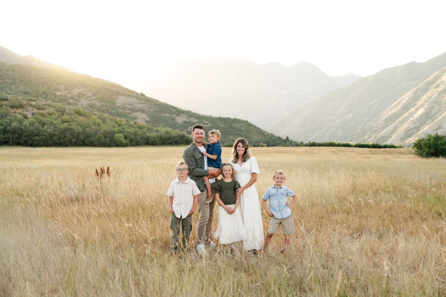 Utah family photographer takes family portraits in a mountain meadow during golden hour. Neutral outfits featuring cream, greens and denim.