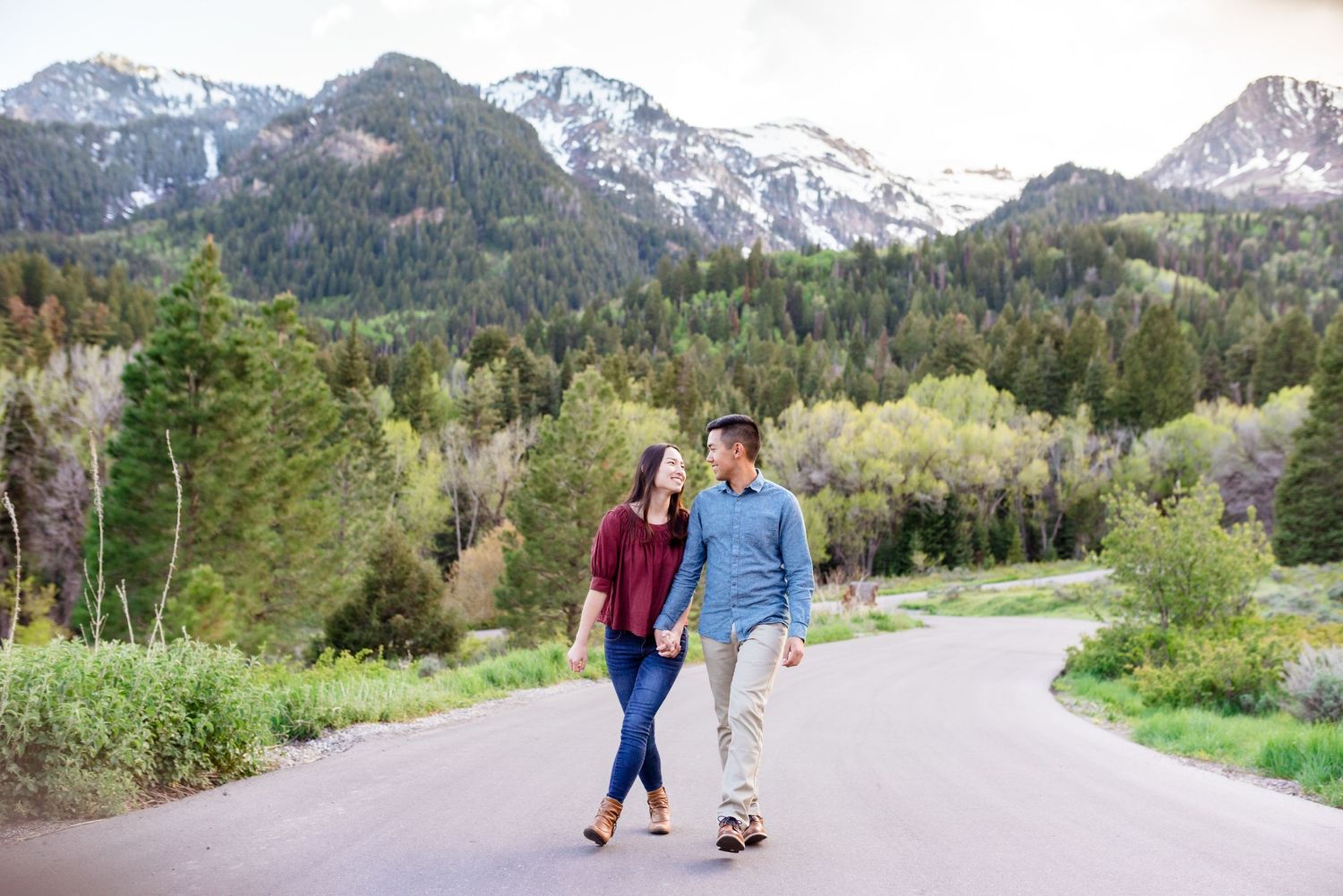 A couple takes a romantic stroll on a mountain path with snow-capped peaks in the background.