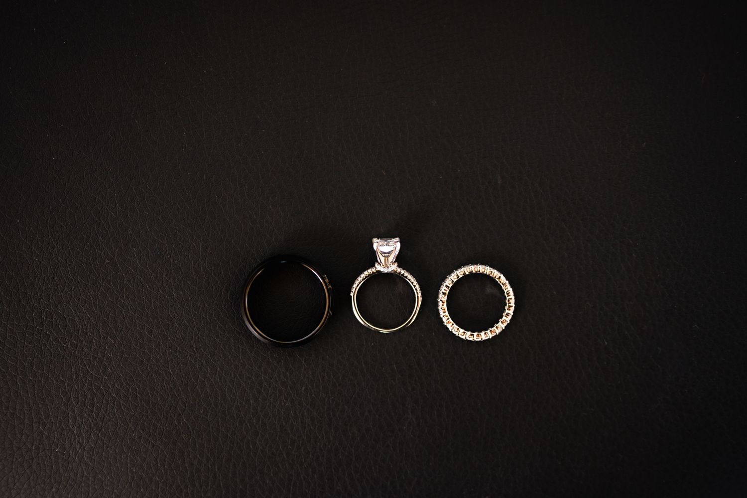 Three wedding rings arranged on dark background showing engagement and wedding bands.