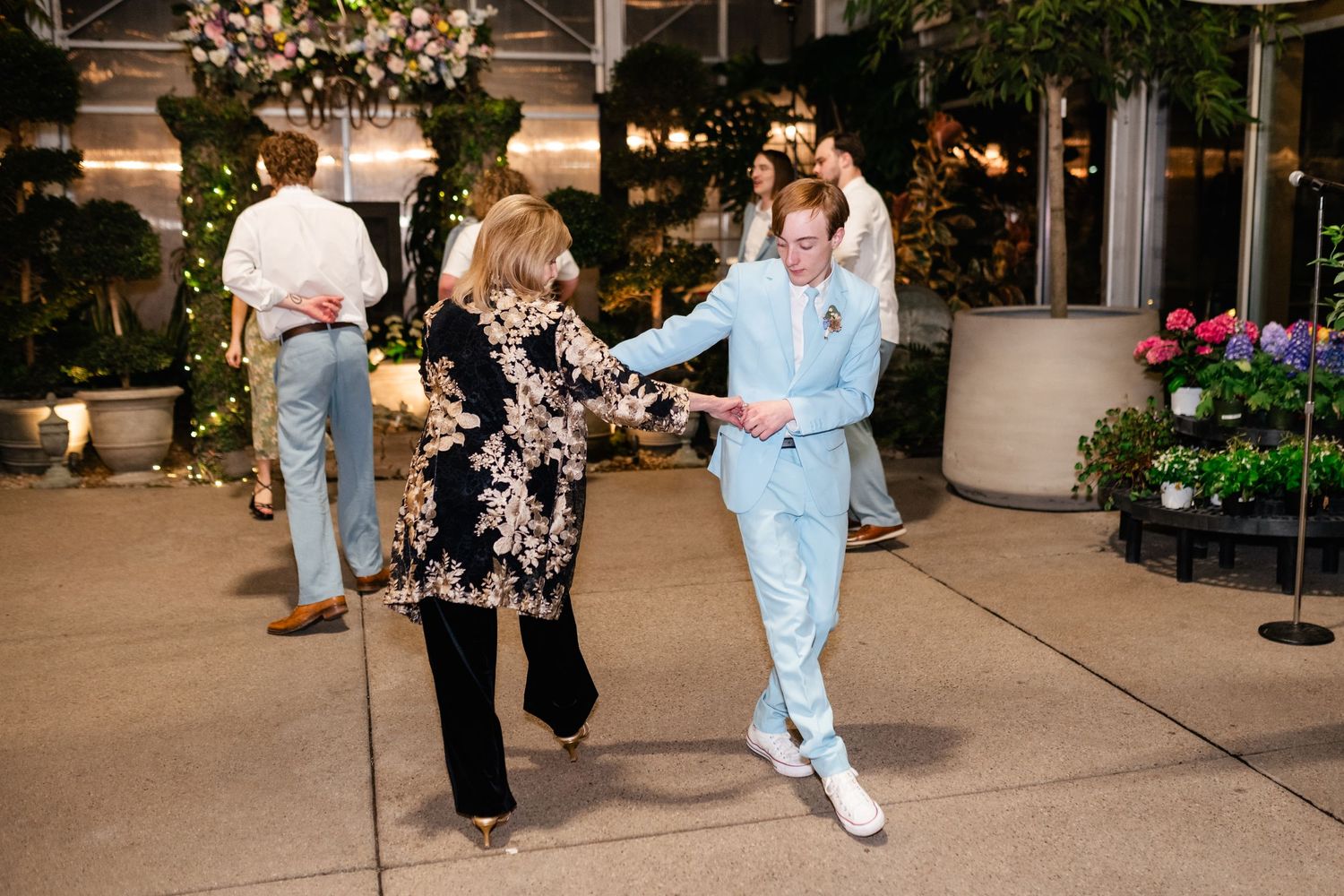 Two people dancing together on a patio with plants and string lights in the evening atmosphere.