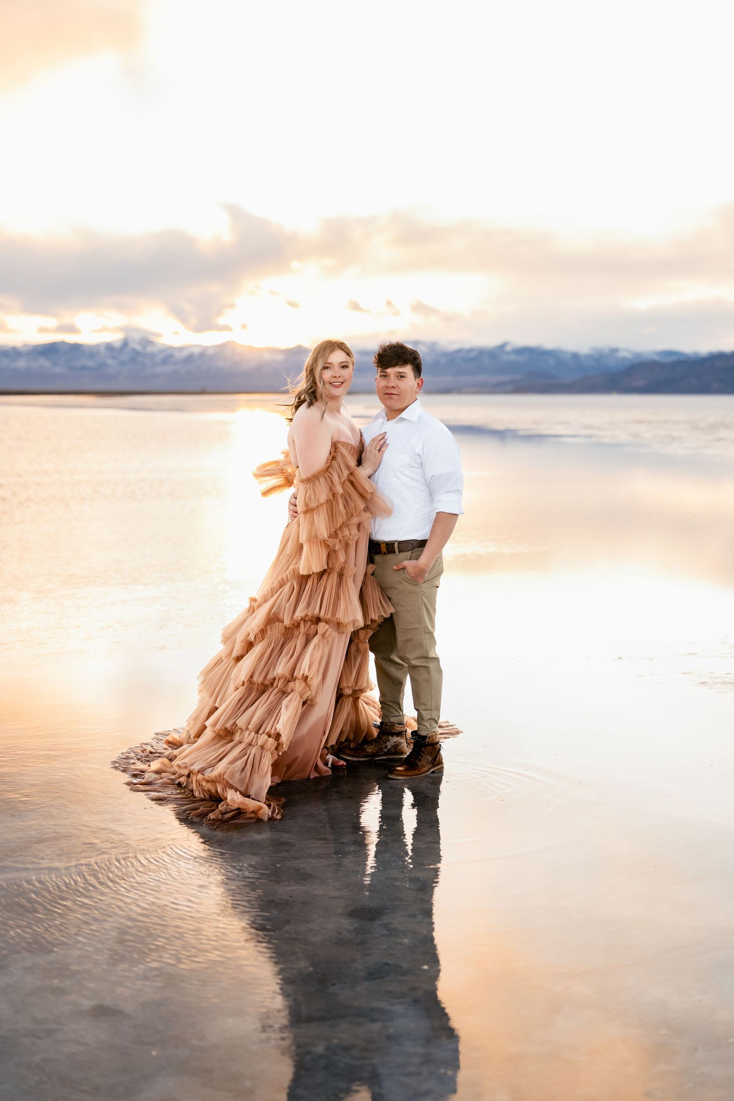 A couple poses together against the surreal backdrop of the flooded Salt Flats during golden hour.