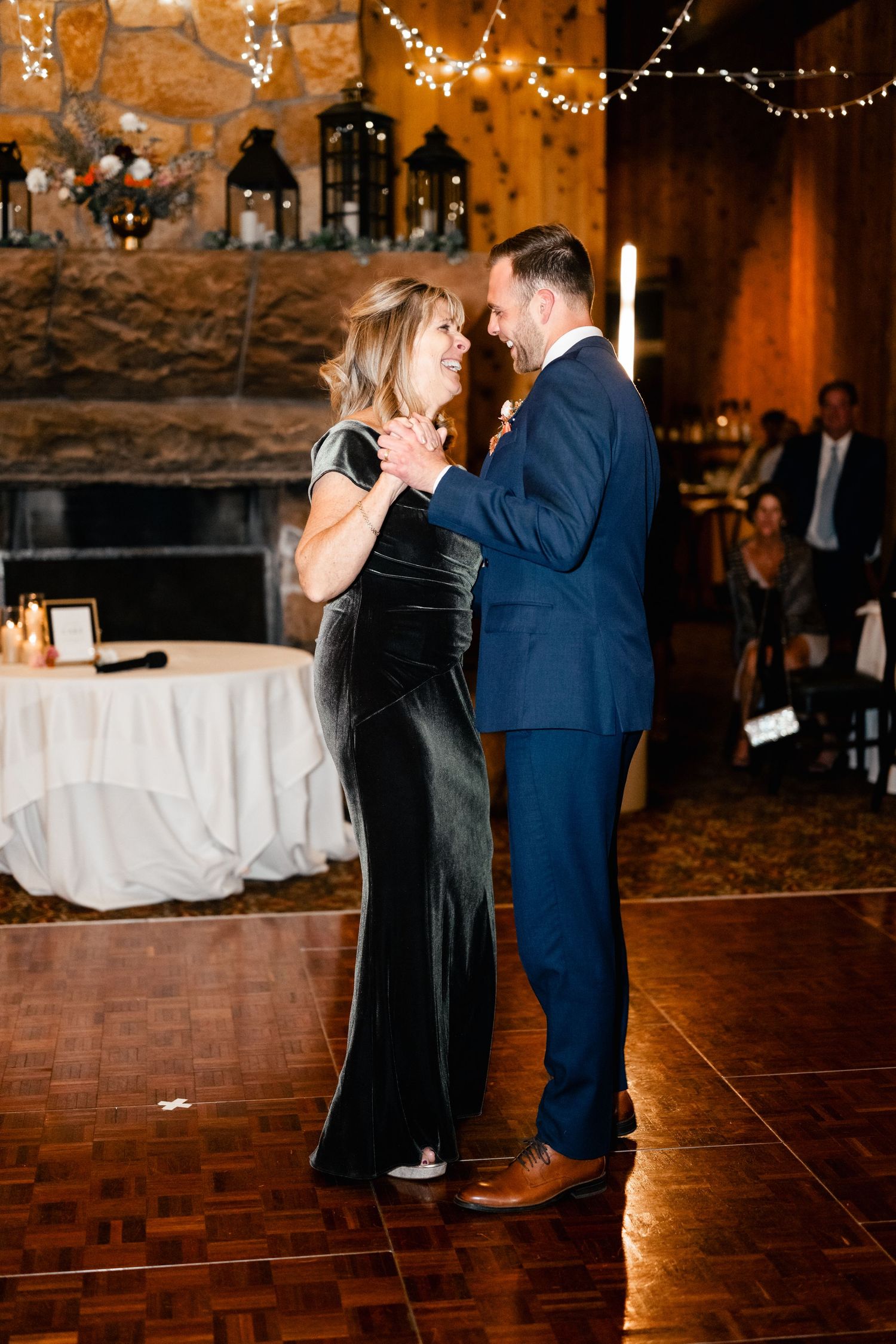 A couple shares their first dance during a wedding reception at a rustic venue decorated with string lights and candles. Park City Wedding.