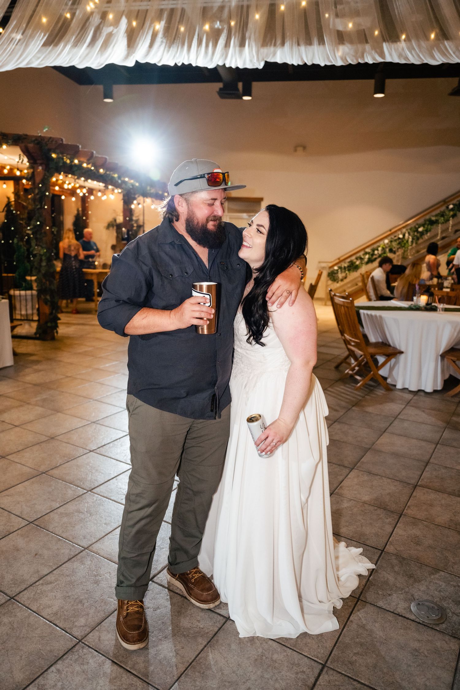 A couple shares an intimate moment at a wedding reception under decorative string lights and draped fabric.