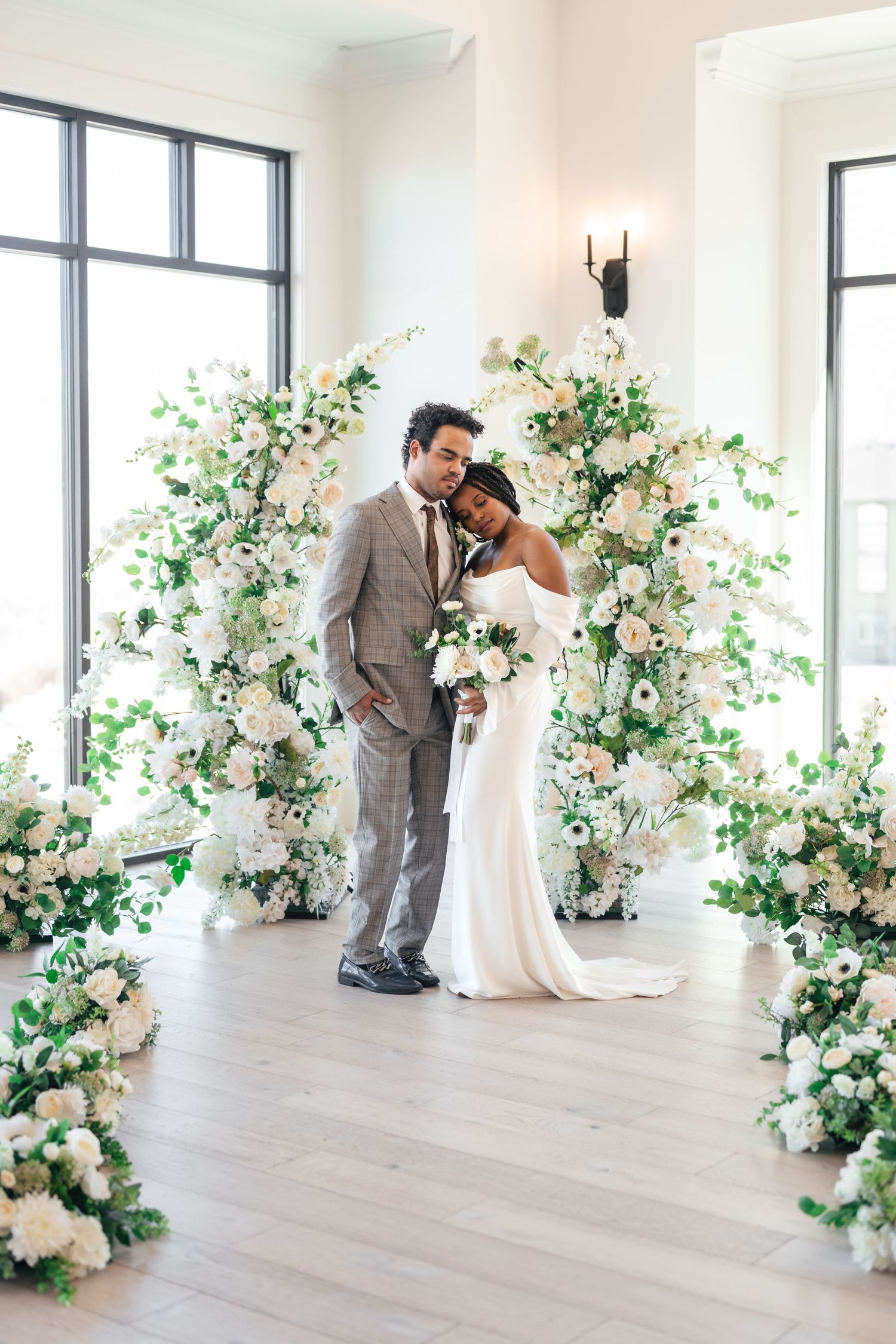 A couple shares an intimate moment in a bright white venue decorated with elegant floral arrangements. Siempre, a Utah County wedding venue.
