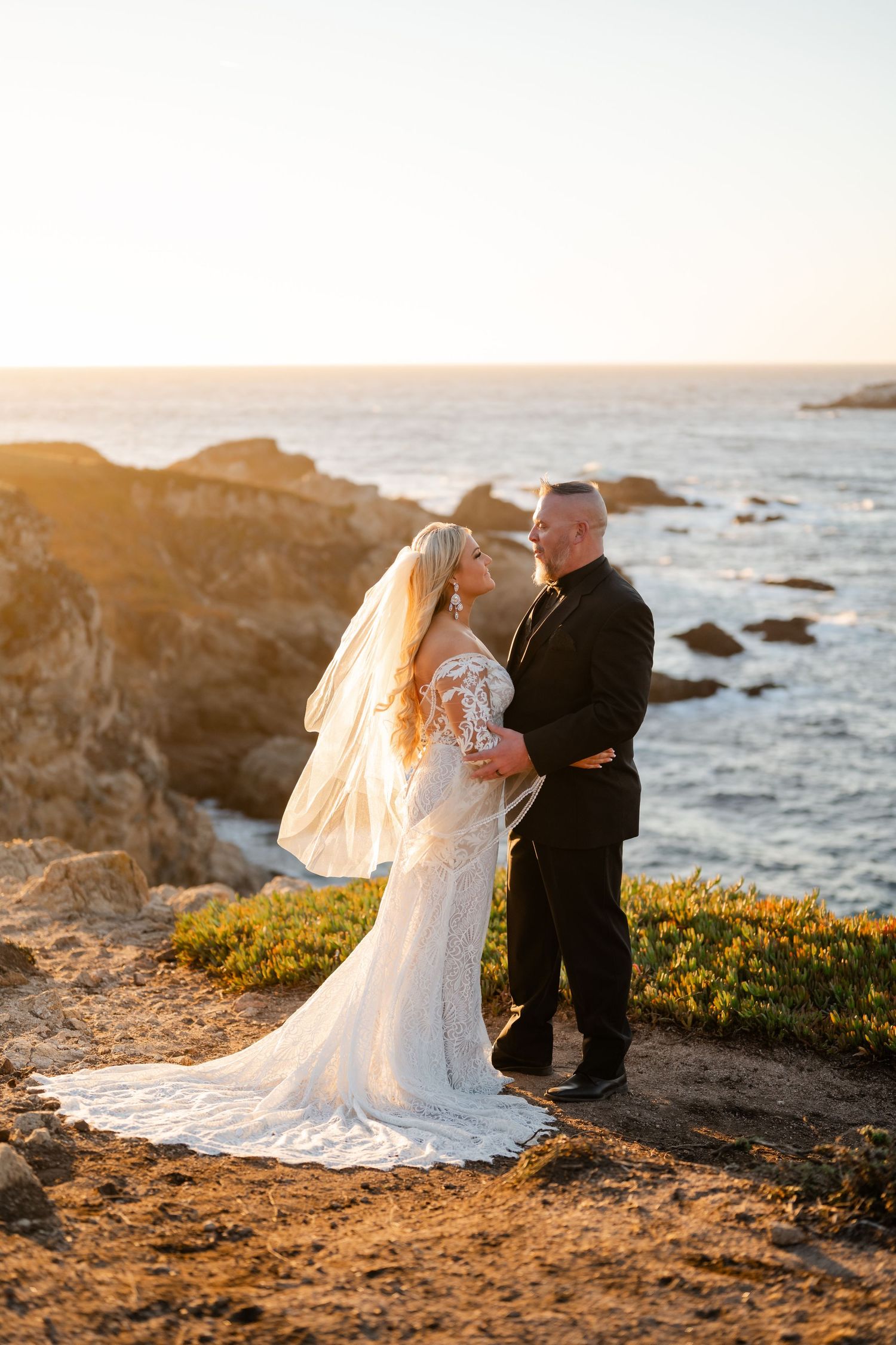 A couple embraces on a scenic coastal overlook during sunset.