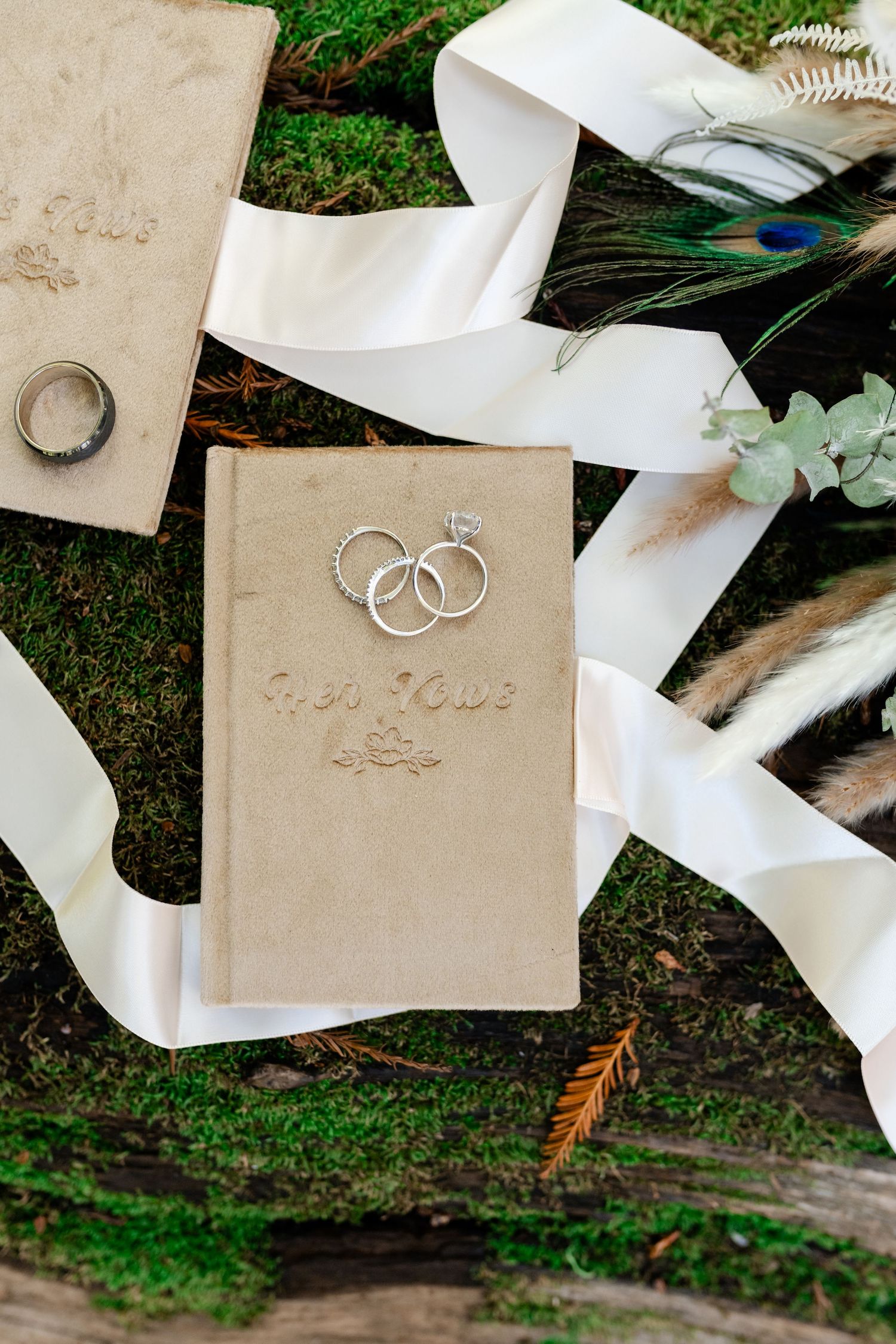 Wedding rings and ribbons displayed on cream-colored cards against mossy forest ground.
