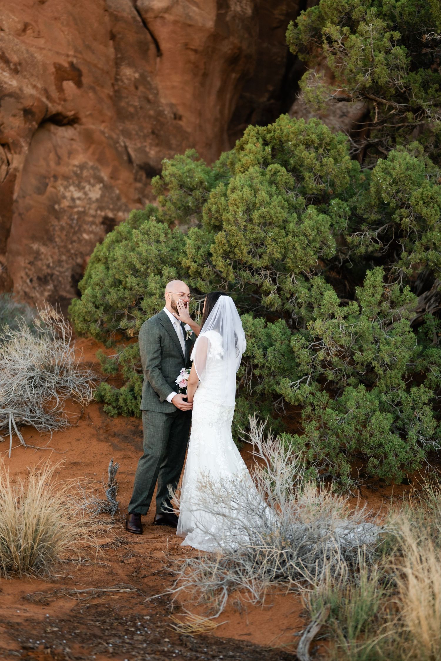An intimate wedding moment photographed against towering red sandstone cliffs and desert flora.