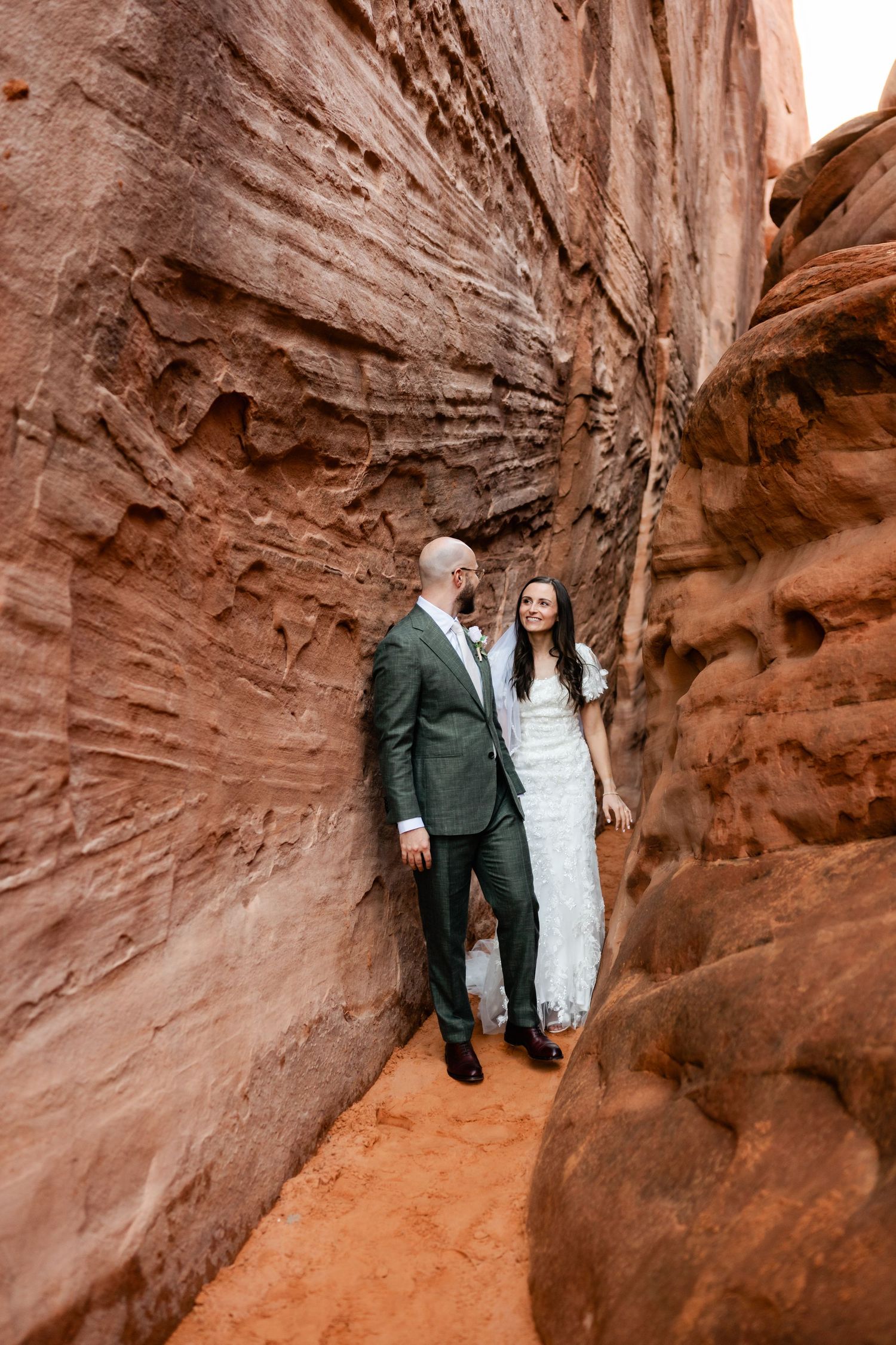 Wedding couple posing between towering red sandstone canyon walls.
