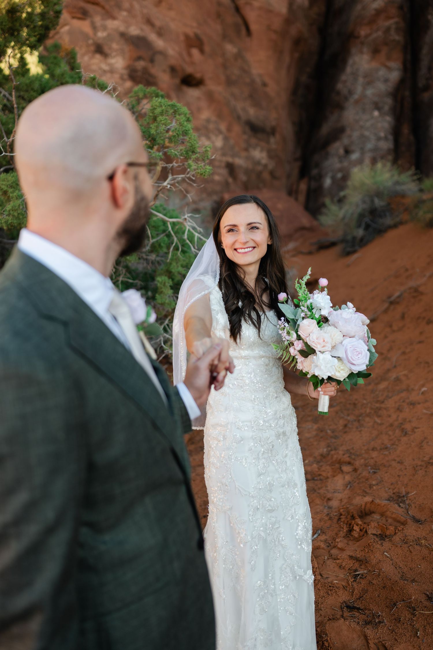 A wedding couple shares a joyful moment against red rock formations in a desert landscape.