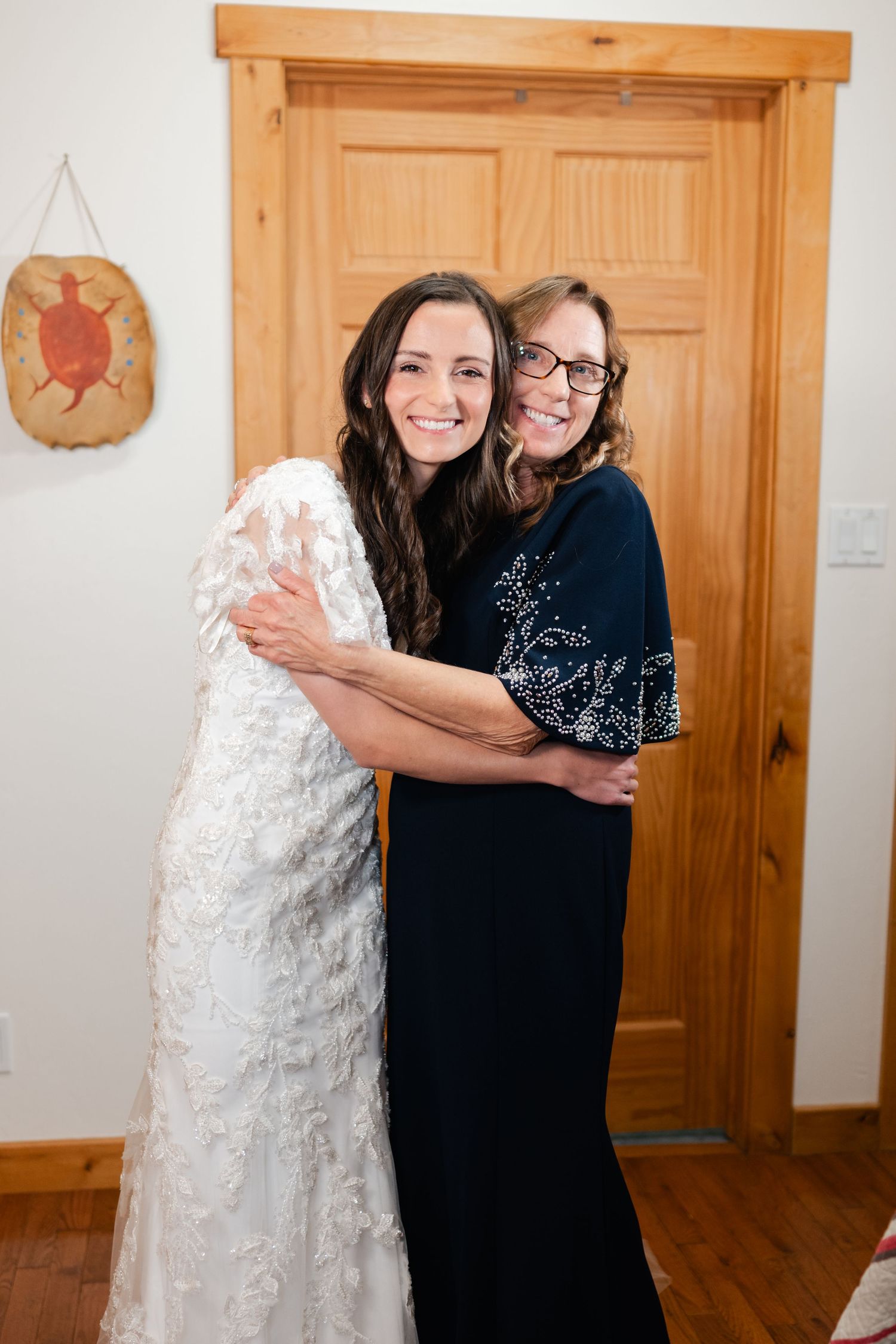 Two people share an emotional embrace during a wedding, one wearing a white lace dress.