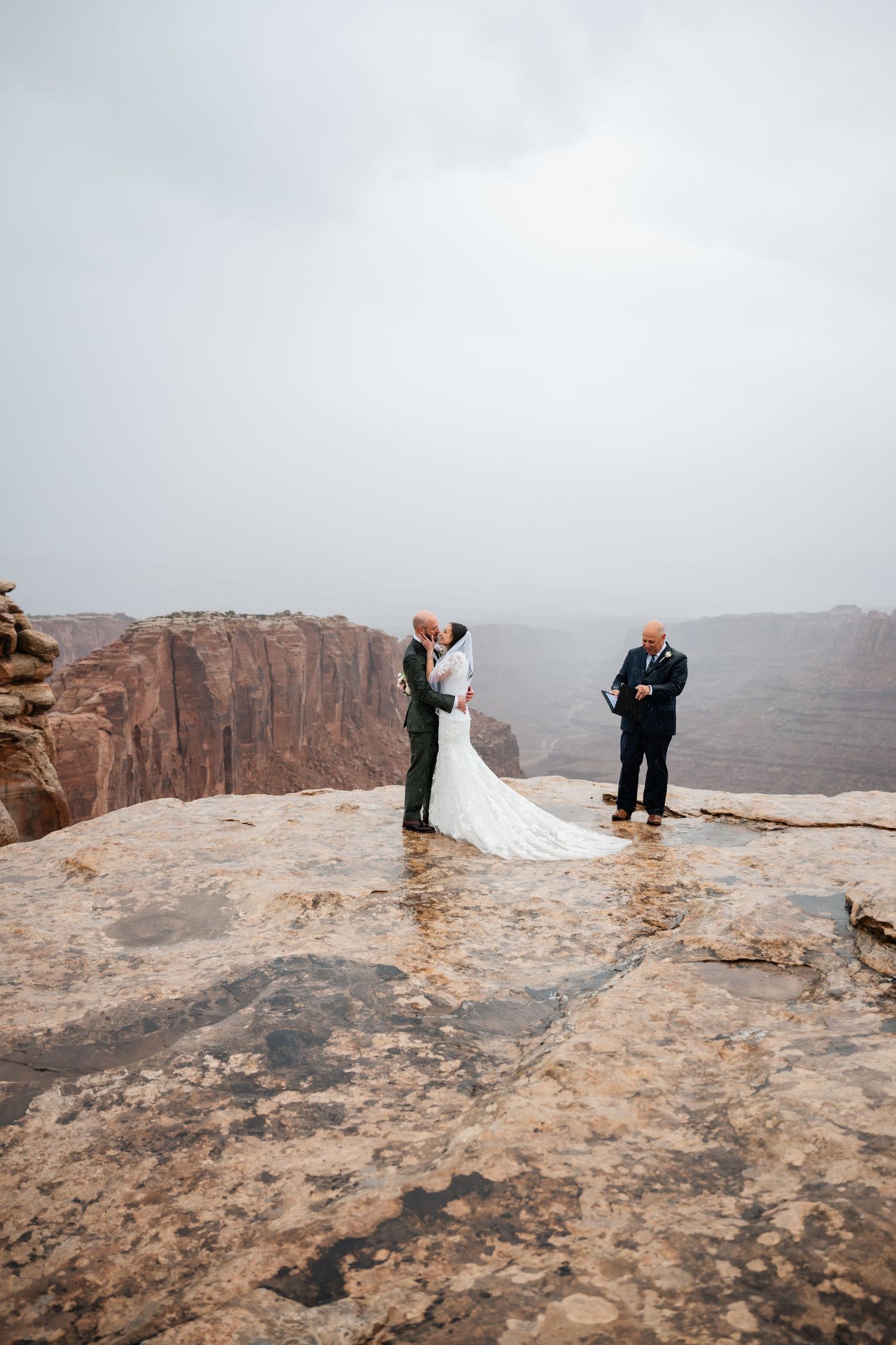 Dramatic desert canyon wedding ceremony with small group gathered on rocky overlook.