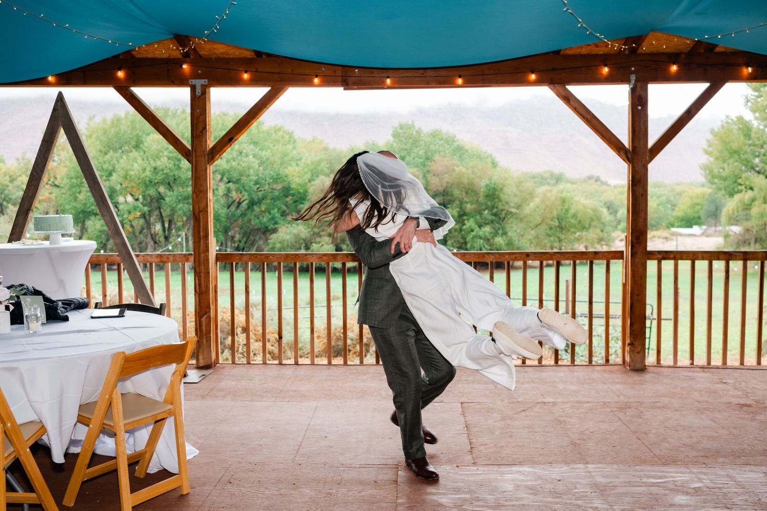 A dance sequence on an outdoor pavilion with string lights and mountain views in the background.